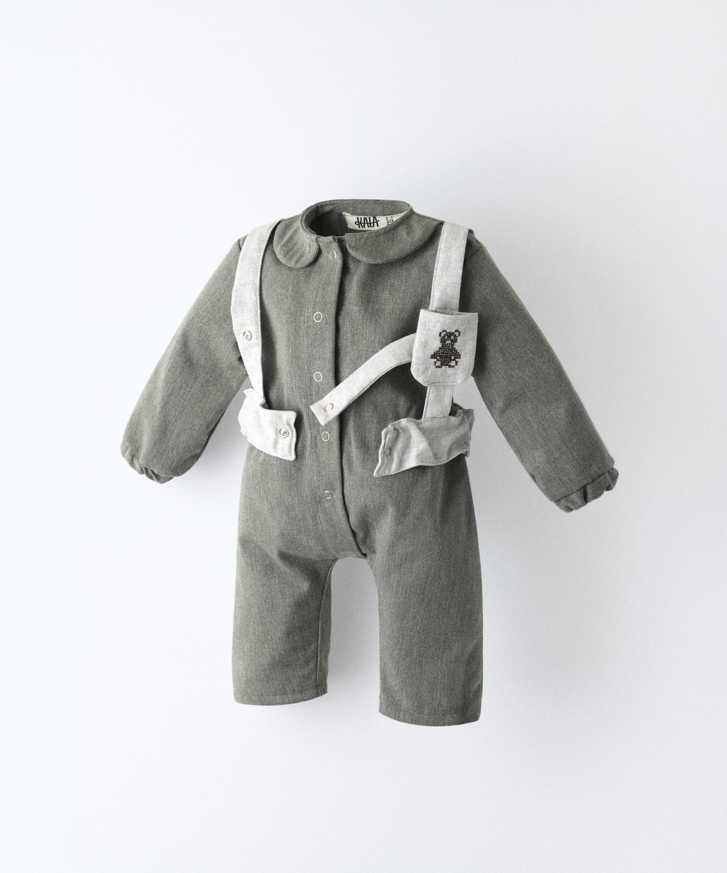 Una pieza icónica. El Jumpsuit Snook en color verde khaki con arnés gris claro y bolsillo. Pieza funcional y atemporal con un diseño único para el bebé.