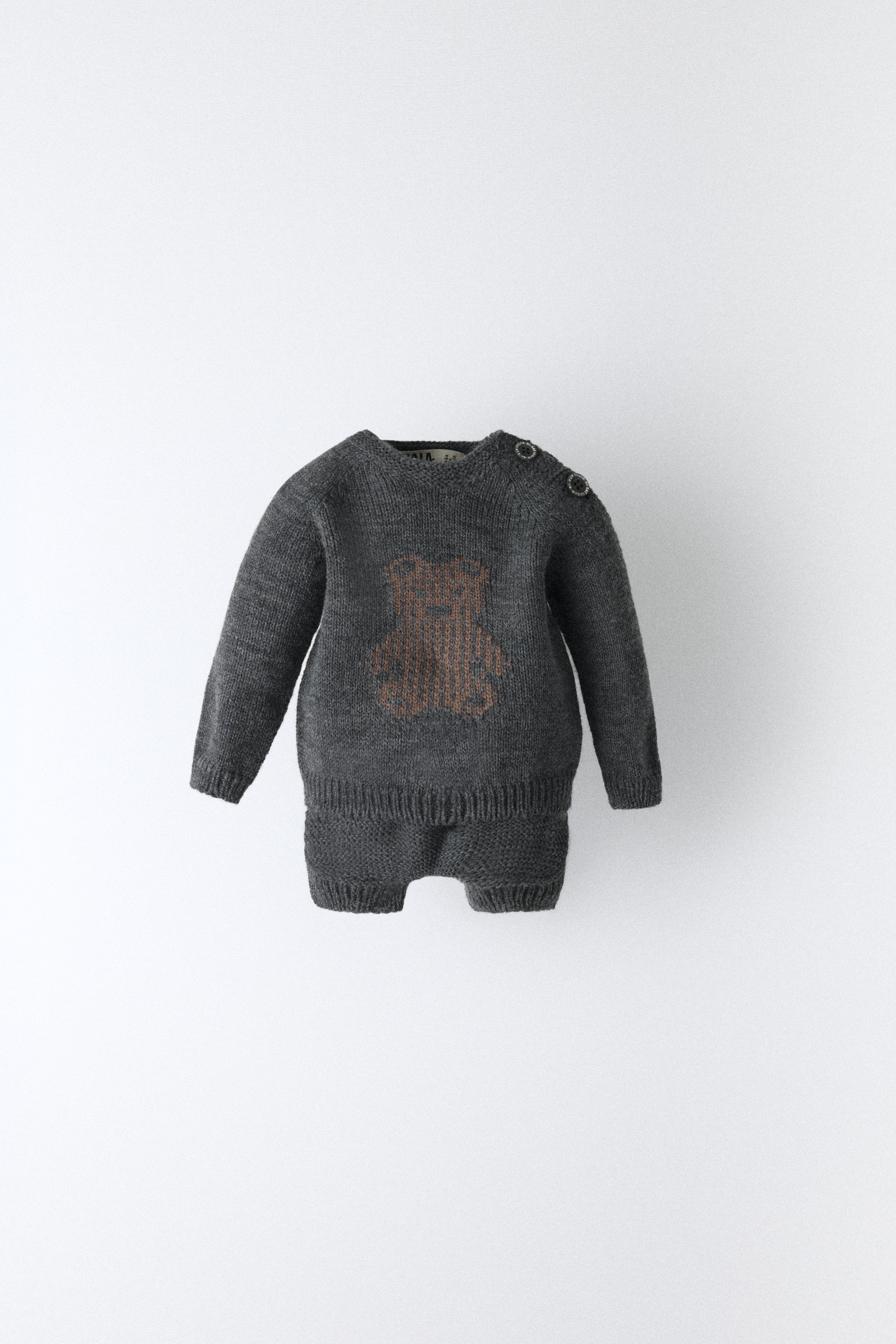 El conjunto Strutt para tu bebé confeccionado en punto acrílico con nuestro oso en contraste marrón en intarsia.