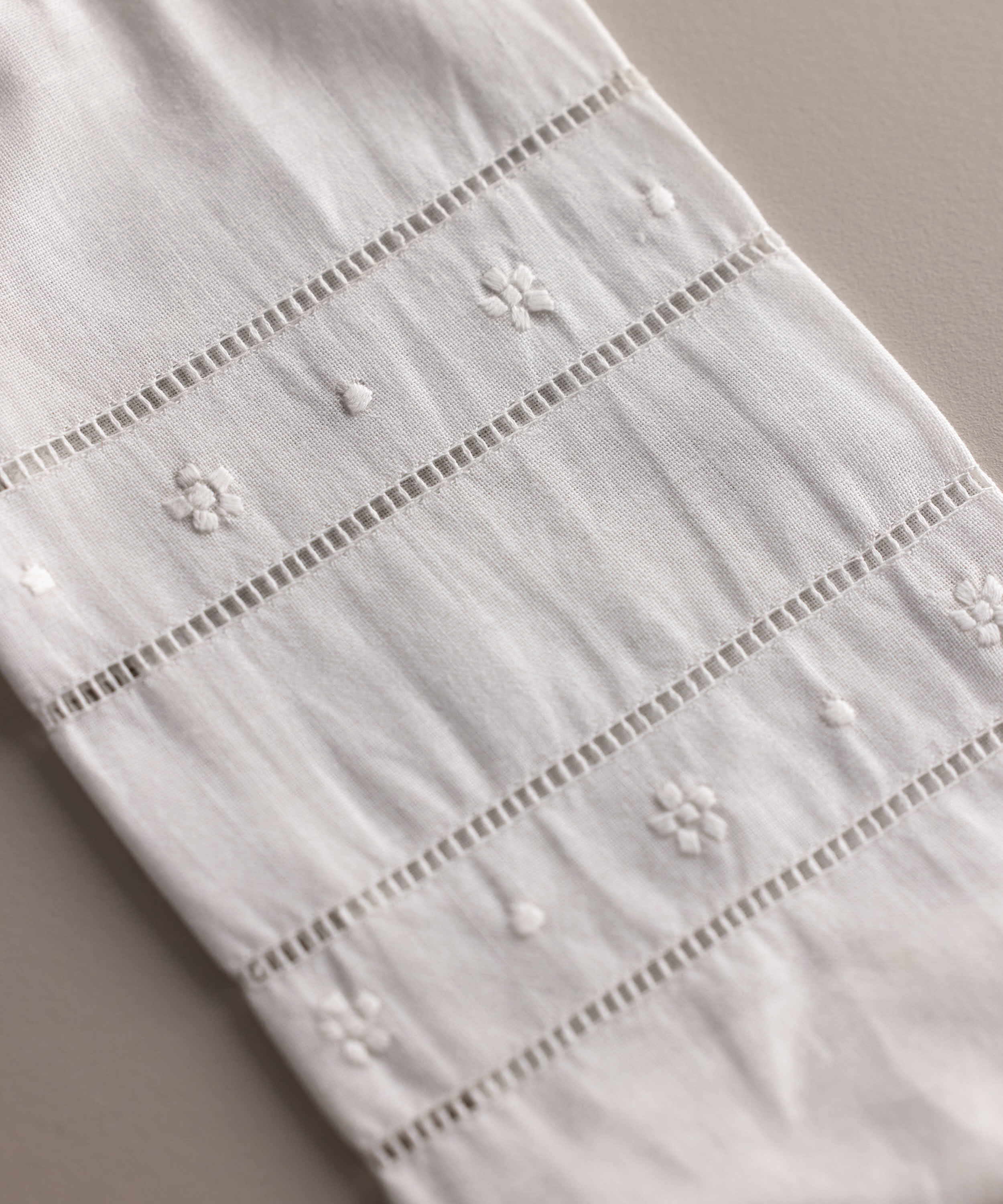 Detalle del bordado floral y vainica en lino beige del set babero y portabiberón artesanal para bebé