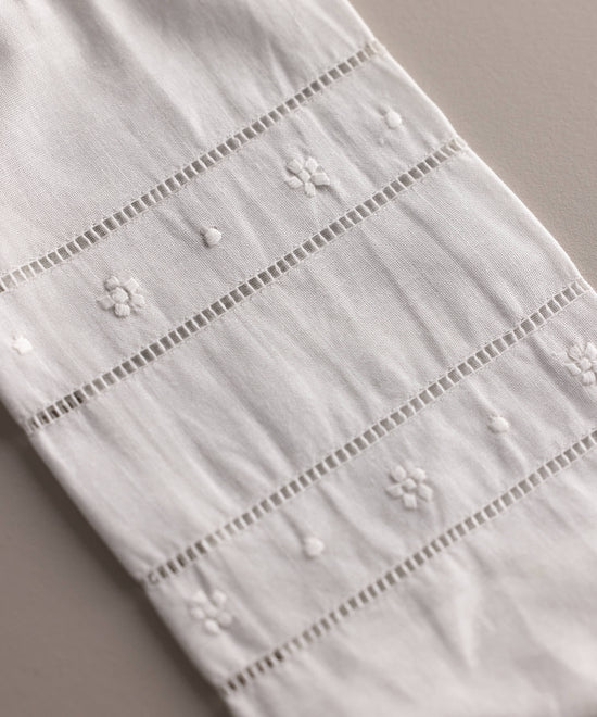 Detalle del bordado floral y vainica en lino beige del set babero y portabiberón artesanal para bebé