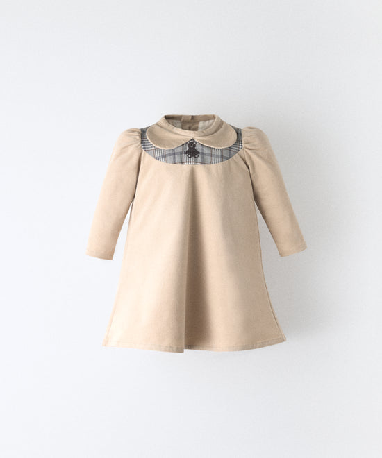 El Faldón Wills beige, confeccionado en pana elástica (97 % algodón BCI / 3 % elastano) con pieza delantera a cuadros y oso kala bordado. Una prenda que celebra los primeros momentos con autenticidad, sensibilidad y estilo atemporal.