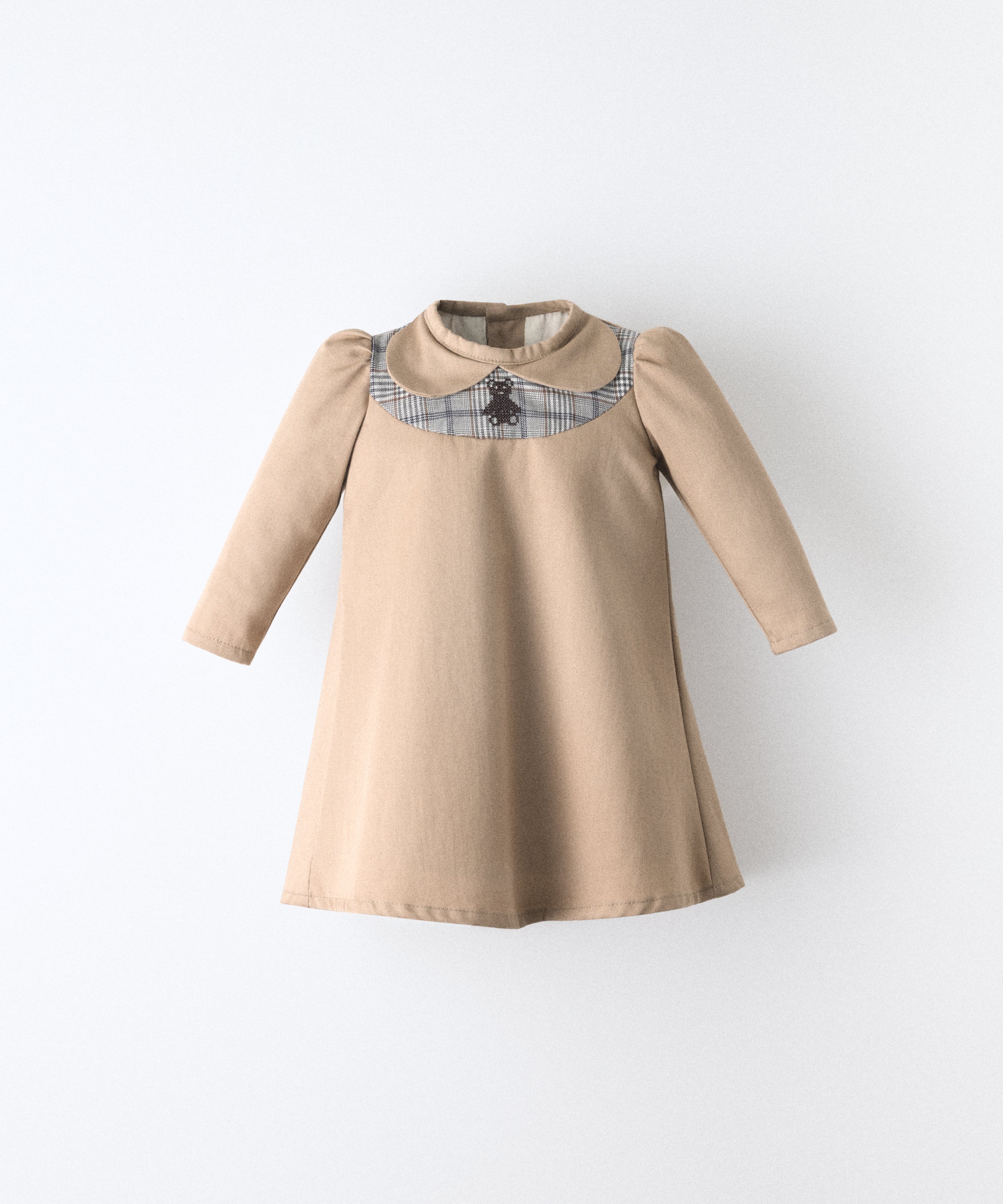 El Faldón Wills avellana, confeccionado en sarga 100 % algodón orgánico certificado GOTS. con pieza delantera a cuadros y oso kala bordado. Una prenda que celebra los primeros momentos con autenticidad, sensibilidad y estilo atemporal.