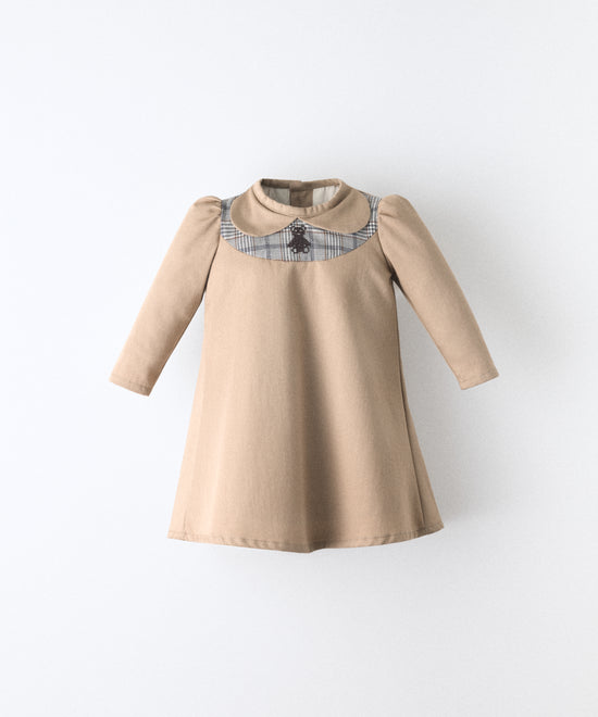 El Faldón Wills avellana, confeccionado en sarga 100 % algodón orgánico certificado GOTS. con pieza delantera a cuadros y oso kala bordado. Una prenda que celebra los primeros momentos con autenticidad, sensibilidad y estilo atemporal.