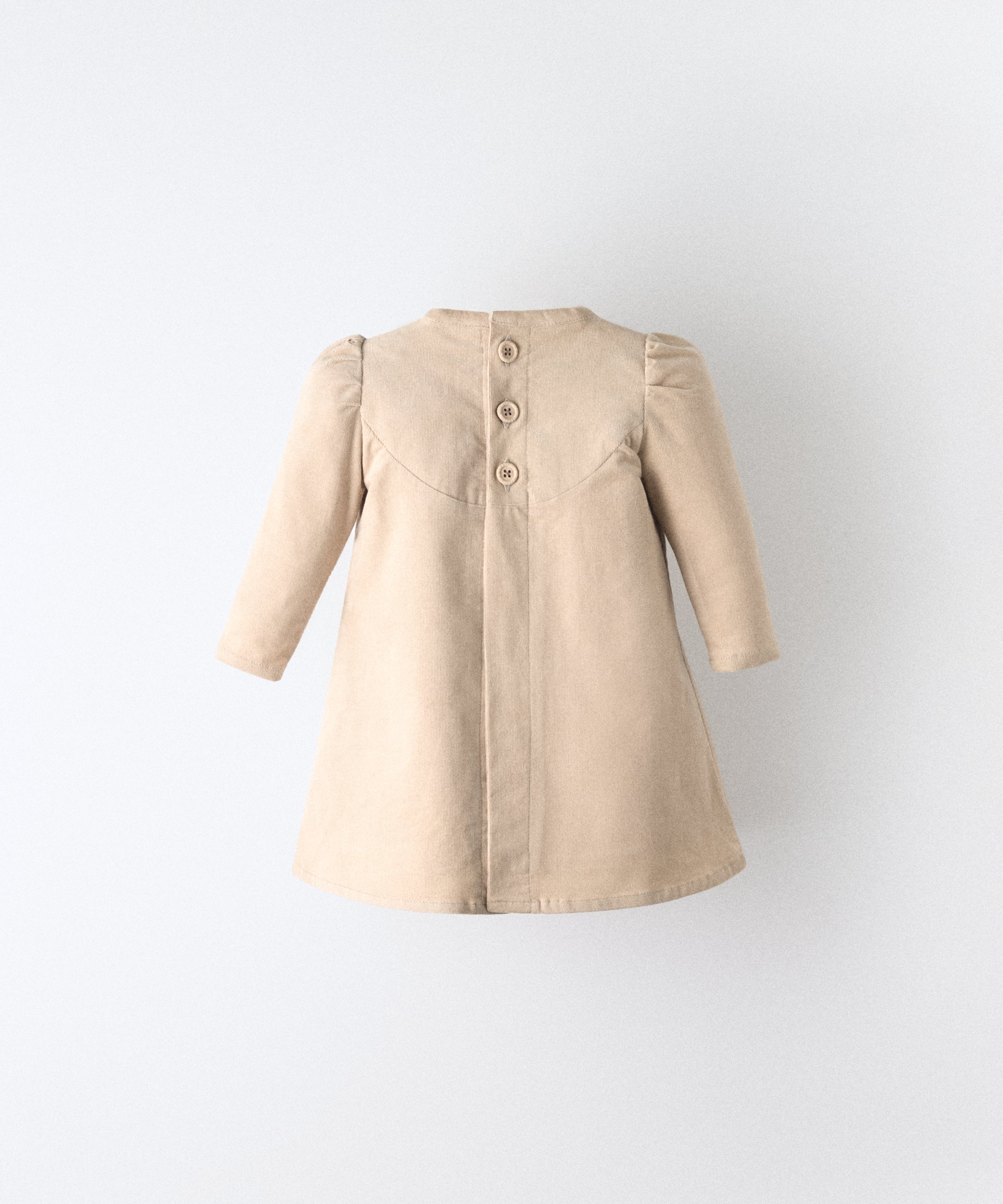 El Faldón Wills beige visto de espaldas, confeccionado en pana elástica (97 % algodón BCI / 3 % elastano) y apertura total central con cierre con botones OEKO TEX en la parte superior. Una prenda que celebra los primeros momentos con autenticidad, sensibilidad y estilo atemporal.