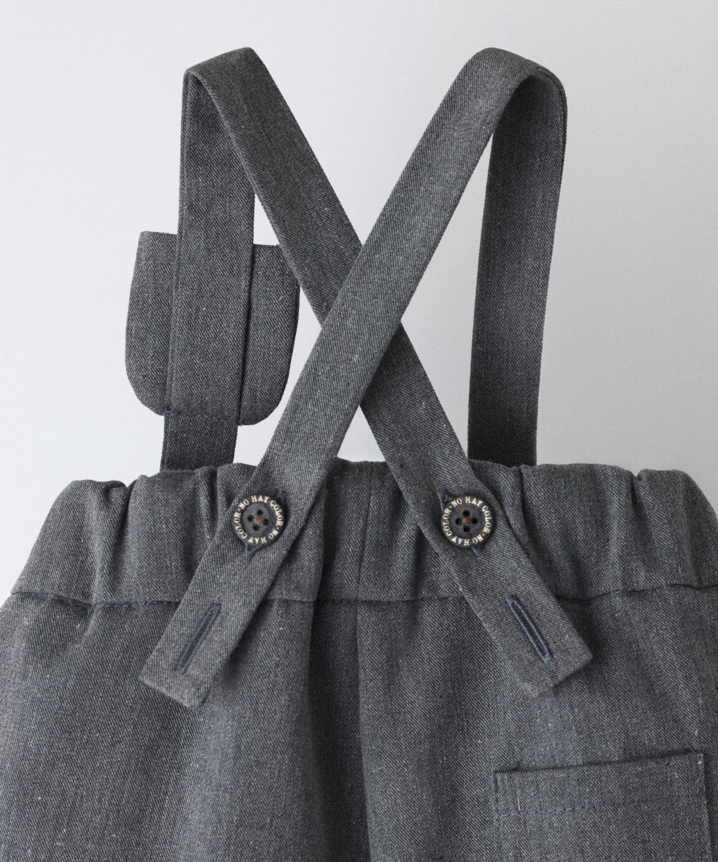 Vista trasera del pantalón bebé gris azulado con tirantes cruzados ajustables con botones oEKO TEX y cintura elástica.