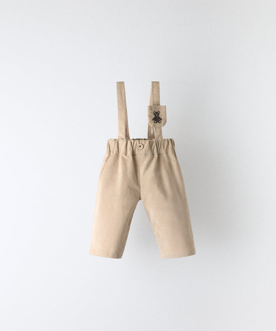 Pantalón bebé beige de pana elástica BCI con tirantes ajustables y bolsillo para chupete Kala.