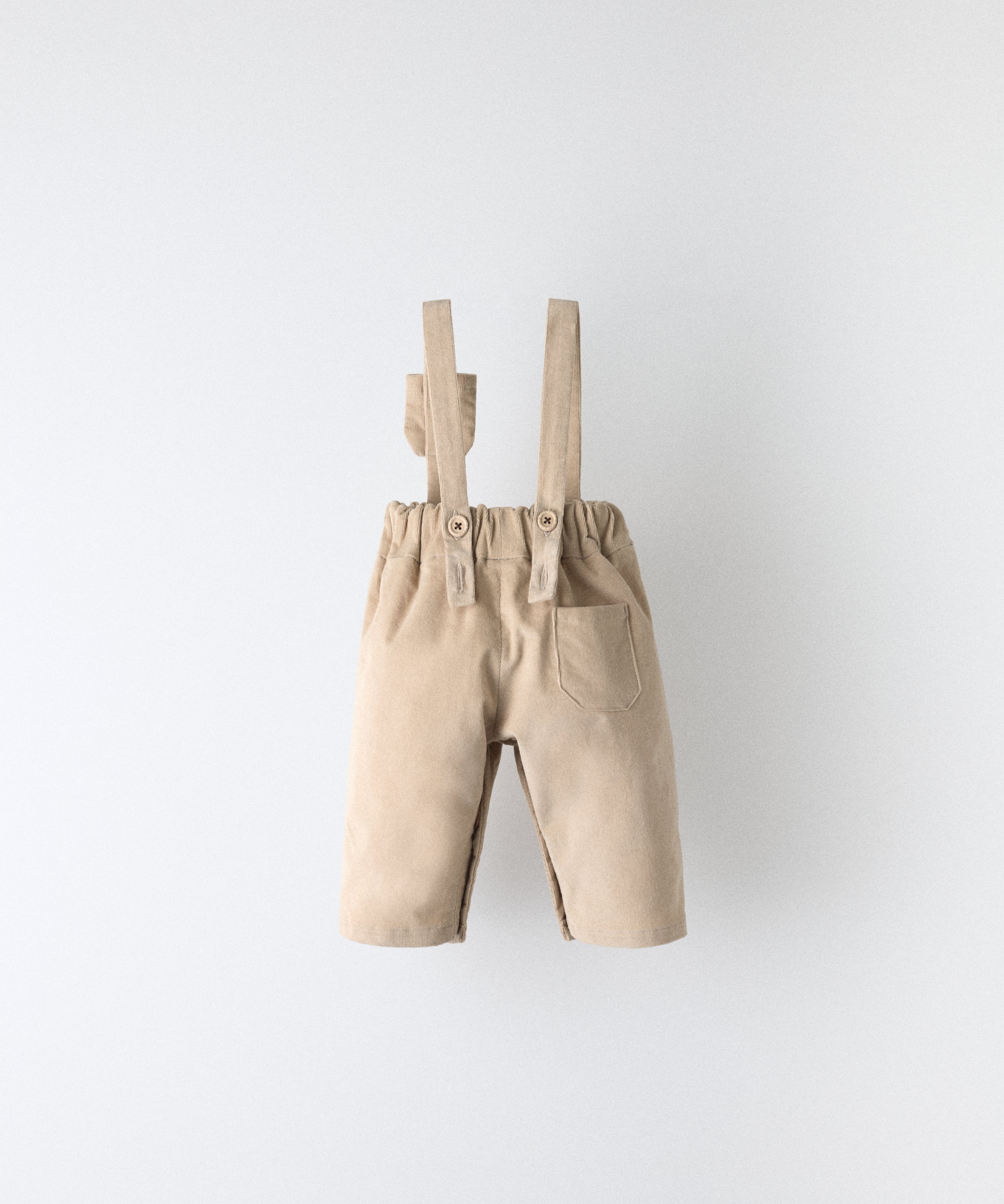 Vista trasera del pantalón bebé beige de pana con tirantes rectos y cintura elástica.