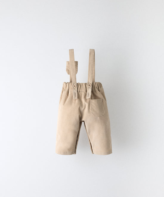 Vista trasera del pantalón bebé beige de pana con tirantes rectos y cintura elástica.