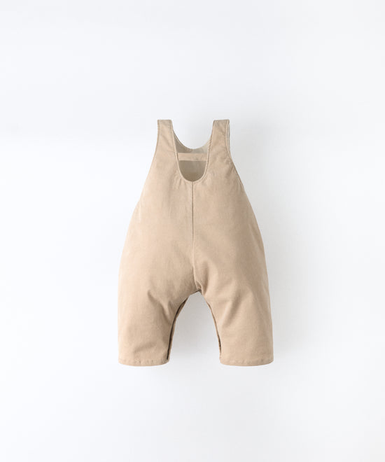 Vista trasera del peto bebé beige de pana elástica con tirantes ajustables. Silueta efecto globo.