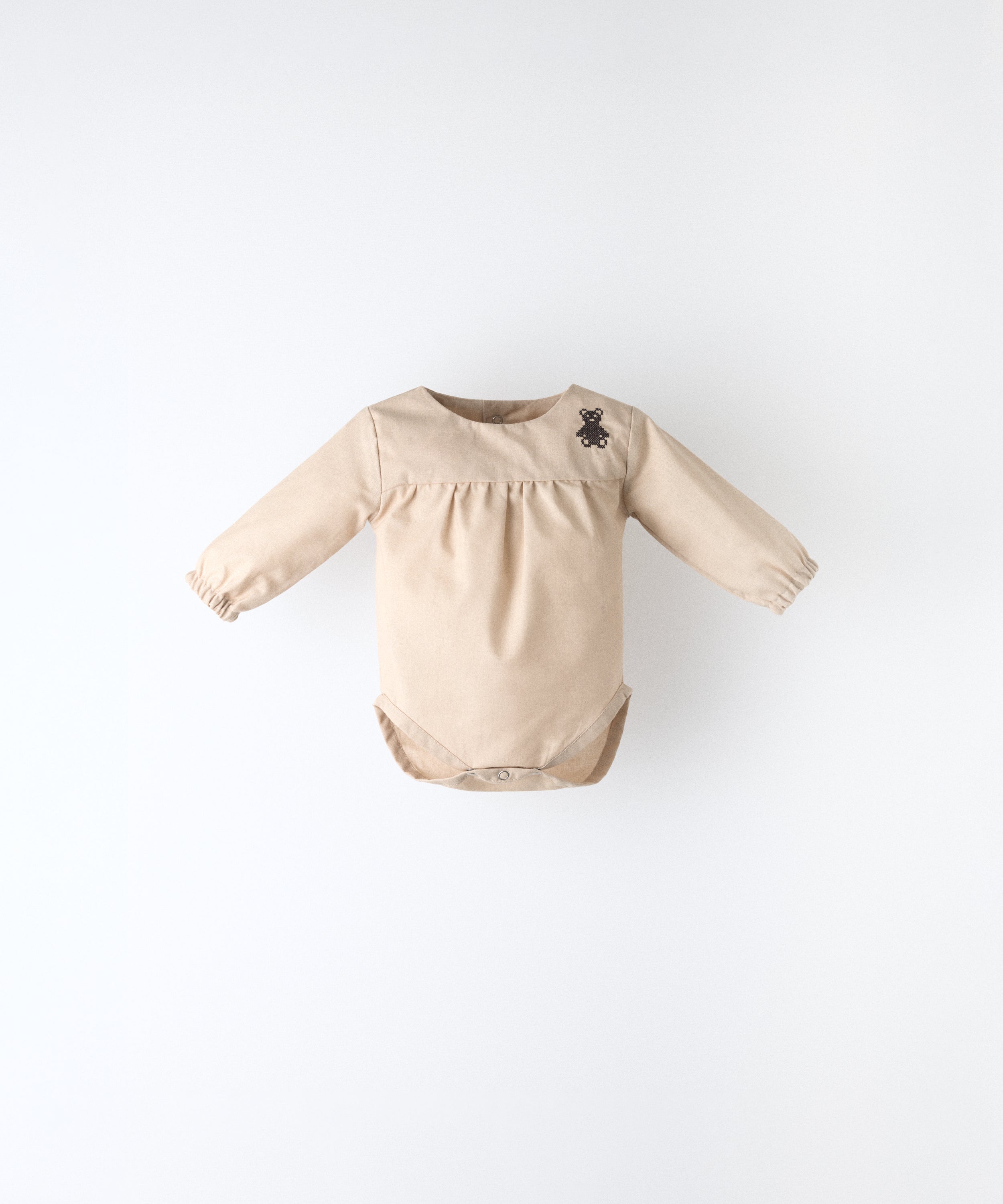 Delantero del body Liberty en manga larga y color arena blanqueada. Confeccionado en 100 % algodón orgánico certificado GOTS y oso de Kala bordado en canesú. Suavidad y cuidado de la piel para tu bebé. www.kala.es