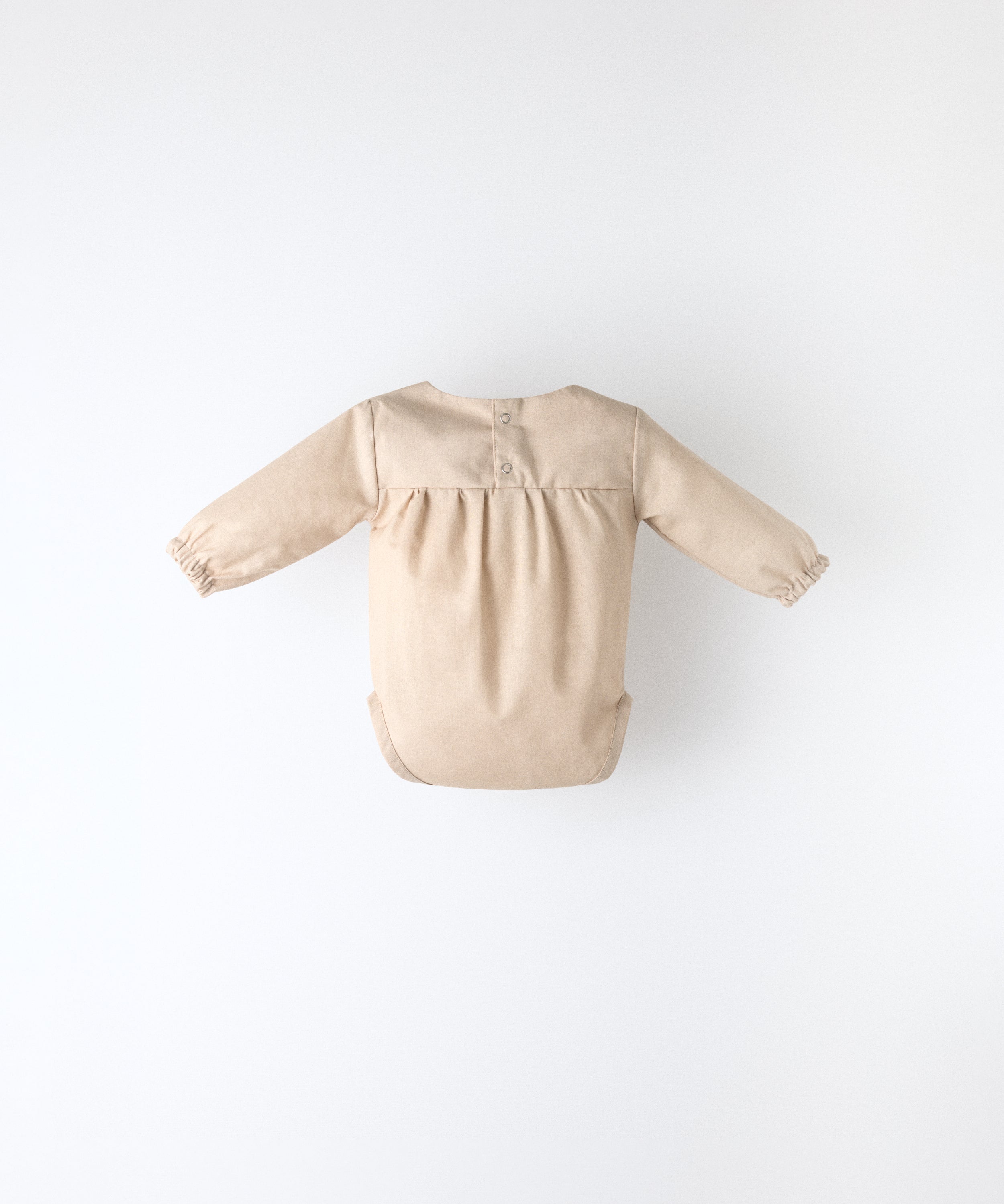 Espalda del body Liberty en manga larga y color arena blanqueada. Confeccionado en 100 % algodón orgánico certificado GOTS, apertura espalda. Suavidad y cuidado de la piel para tu bebé. www.kala.es