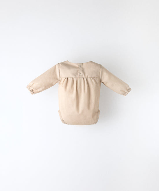 Espalda del body Liberty en manga larga y color arena blanqueada. Confeccionado en 100 % algodón orgánico certificado GOTS, apertura espalda. Suavidad y cuidado de la piel para tu bebé. www.kala.es