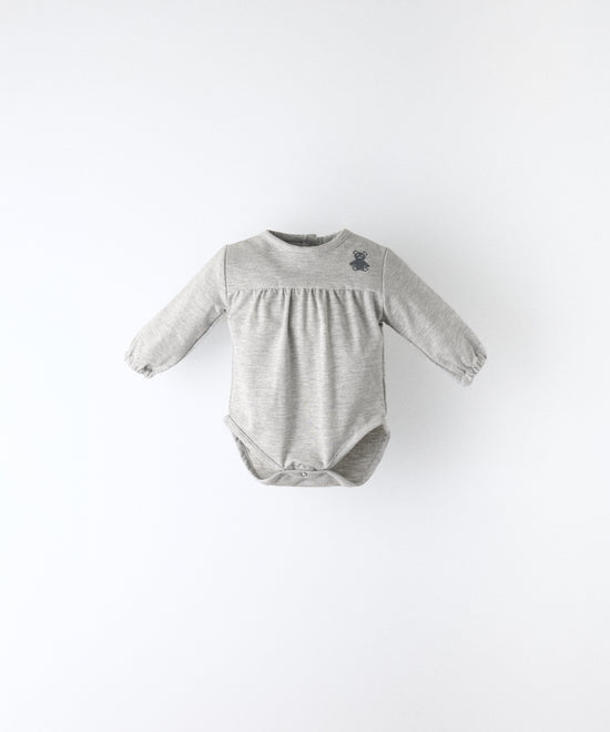 Delantero del Body Liberty en manga larga y color gris claro. Confeccionado en punto 97 % algodón orgánico + 3 % elastano, certificado GOTS. Suavidad y cuidado de la piel para tu bebé. www.kala.es