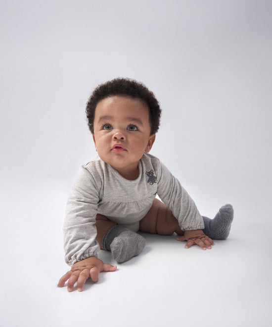 Modelo bebé con El Body Liberty Gris Claro. Confeccionado en punto 97 % algodón orgánico + 3 % elastano, certificado GOTS. Suavidad y cuidado de la piel para tu bebé. www.kala.es