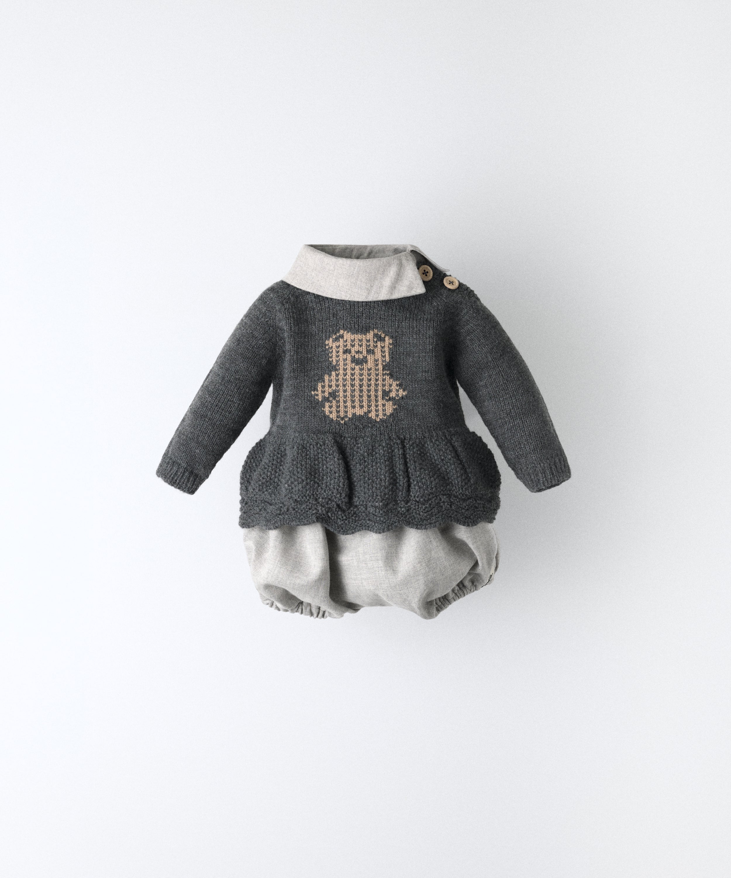 El Conjunto Bloomer consta de un vestido y un pantalón bloomer. El vestido de manga larga y punto con oso kala en intarsia color beige.Cuello camisero contrastado en sarga gris clara con apertura lateral. Mismo tejido empleado en pantalón. Autenticidad sin limites para tu bebé. www.kala.es