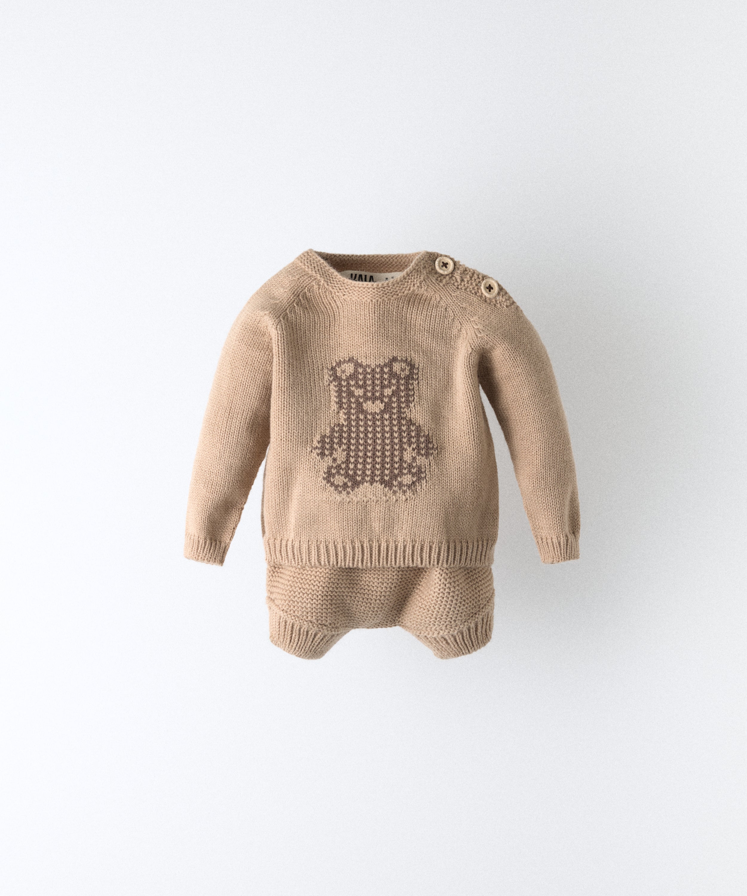 El Conjunto Strutt beige de Kala está compuesto por dos piezas, un pantalón corto y un jersey de manga larga con oso marrón en intarsia. Una fórmula que eleva lo cotidiano desde los primeros pasos. www.kala.es