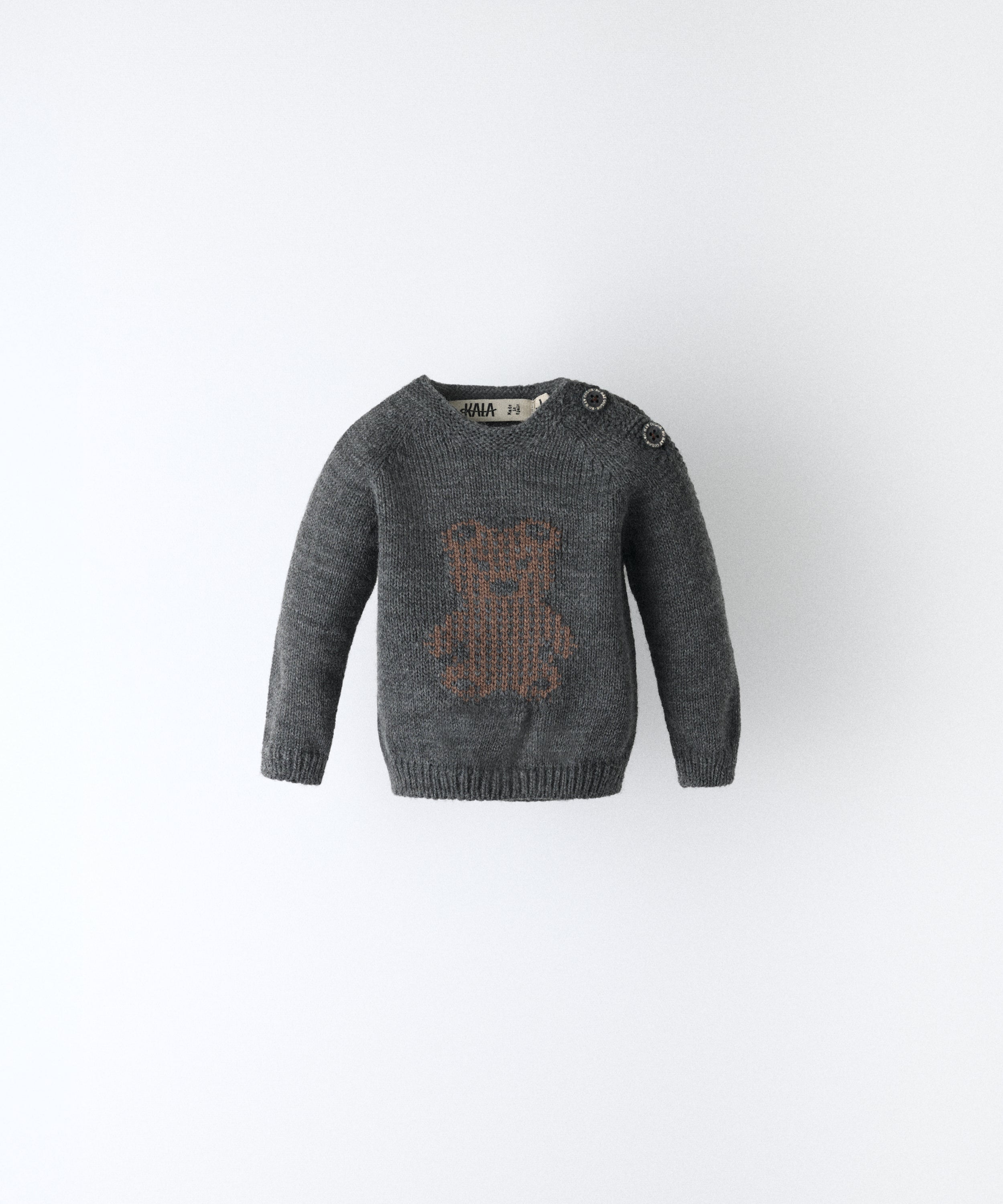 Delantero del Jersey gris oscuro del Conjunto Strutt. Diseño con oso Kala en intarsia marrón y abertura en hombro con cierre botones OEKO TEX al tono. Engomado en puños y cintura. Diseño único para tu bebé. www.kala.es