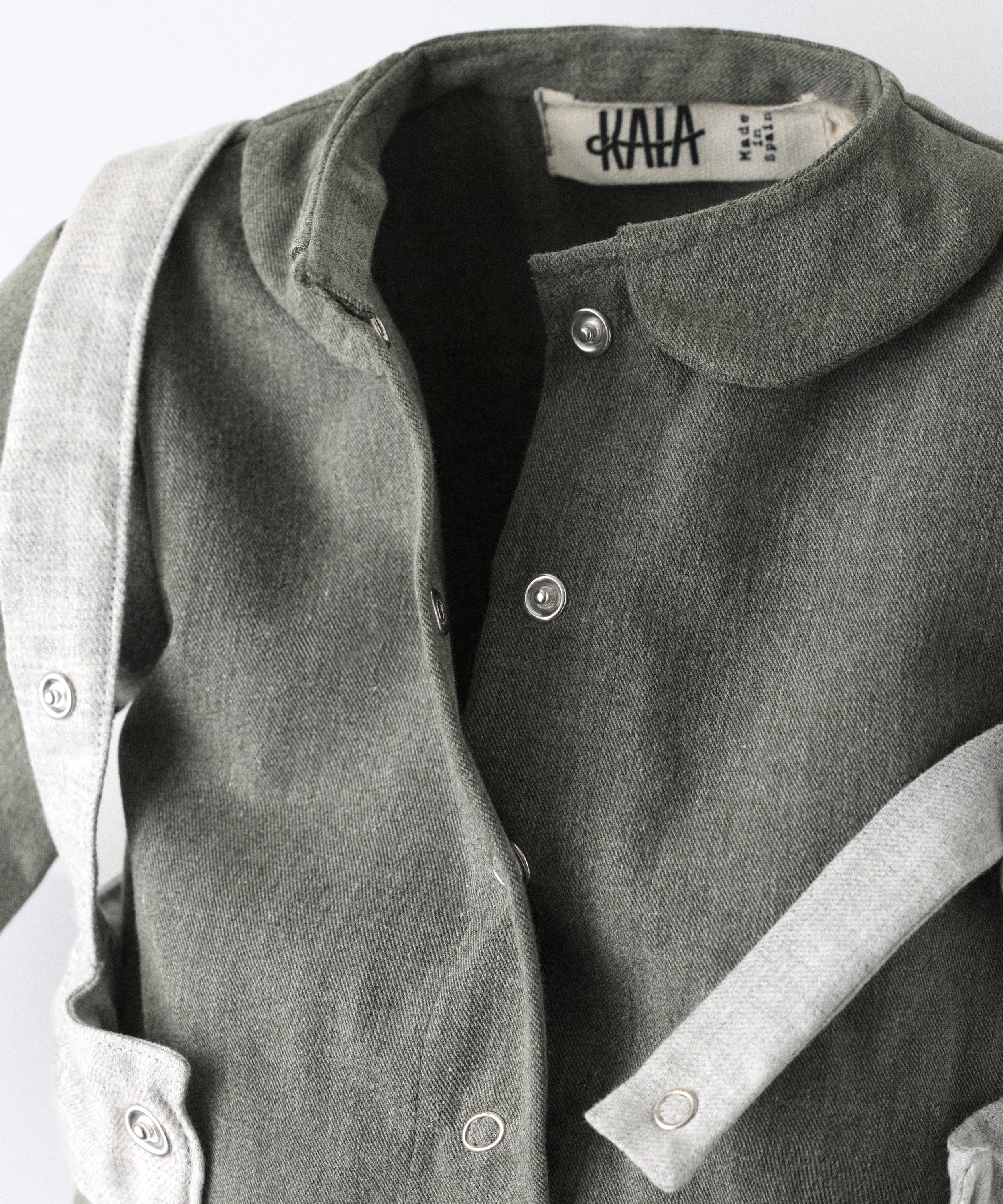 Detalle de cierre delantero con botos automáticos del Jumpsuit Snook verde khaki con arnés abierto. Diseño y atemporalidad para tu bebé. Pensado para acompañar el crecimiento con comodidad y carácter. www.kala.es