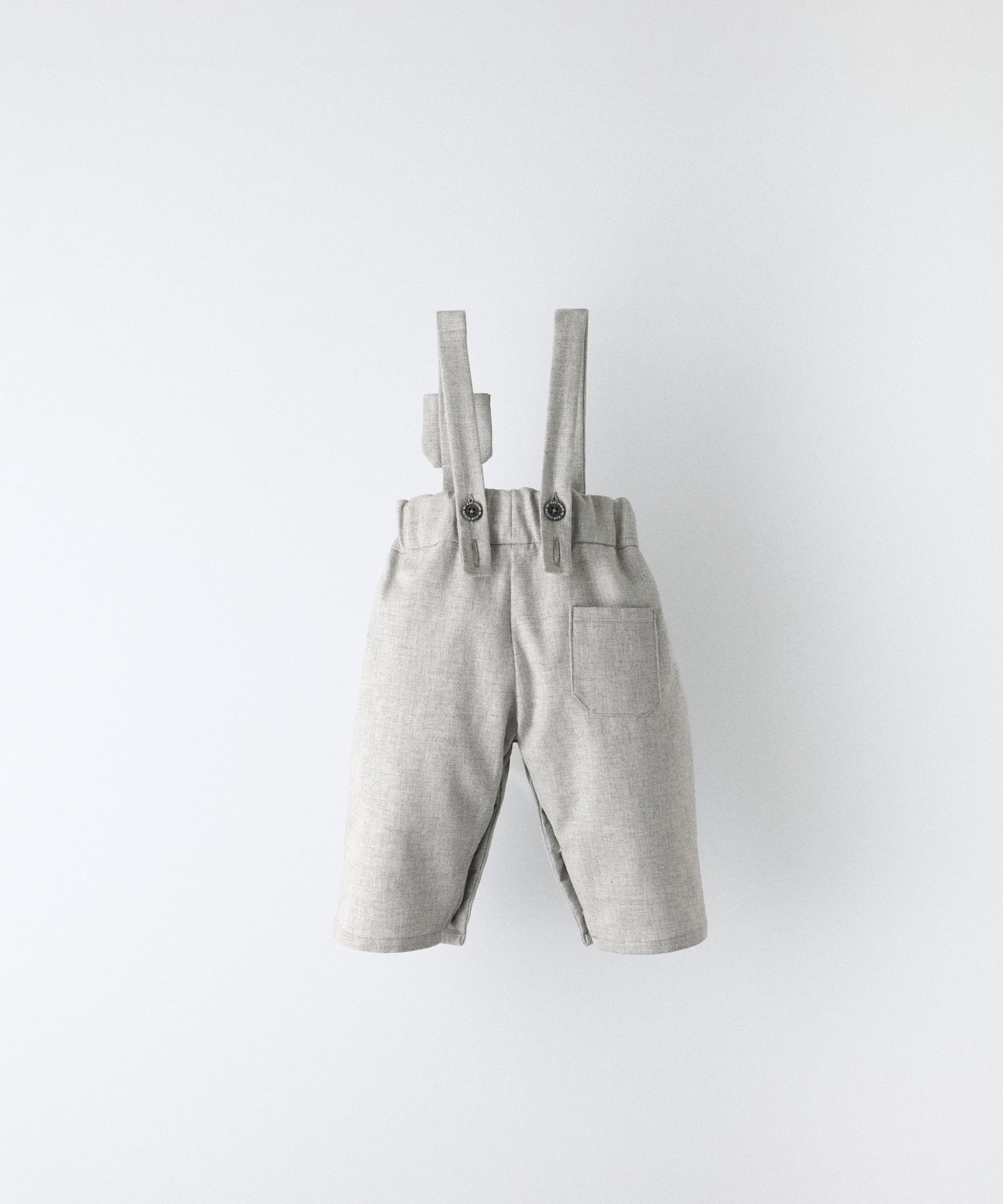 Vista trasera del Pantalón Miller gris claro confeccionado con 100 % algodón BCI. Tirantes ajustables con botón OEKO TEX al contraste. Diseño y versatilidad para tu bebé. www.kala.es