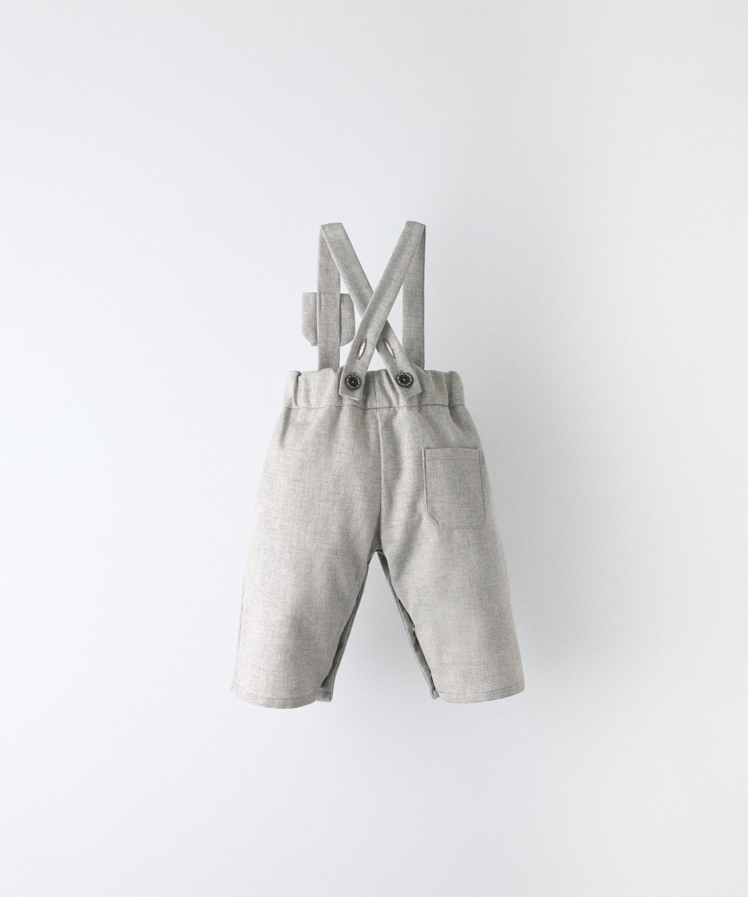 Vista trasera del Pantalón Miller gris claro confeccionado con 100 % algodón BCI. Tirantes cruzados y ajustados con botón OEKO TEX al contraste. Diseño y versatilidad para tu bebé. www.kala.es