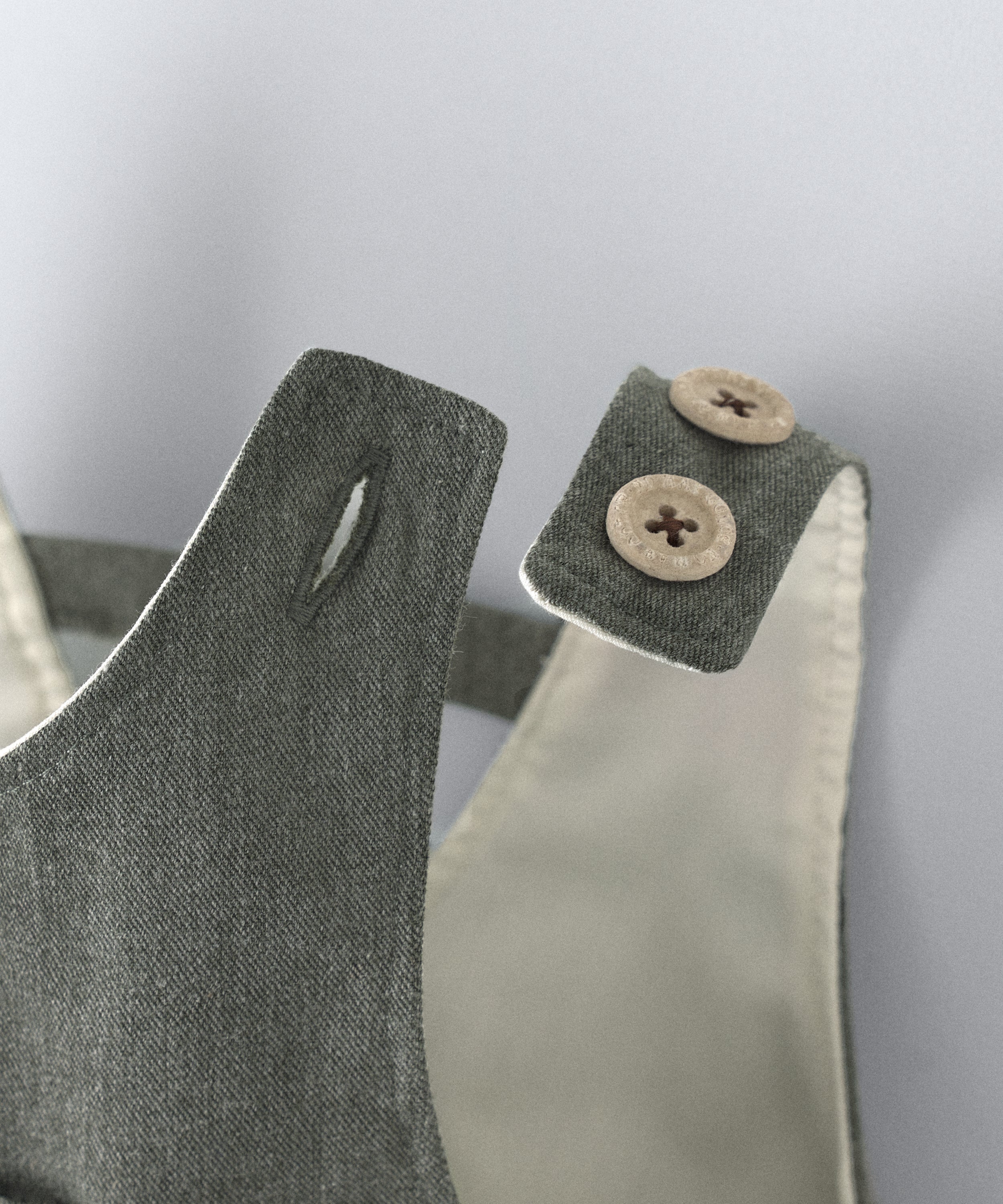 Detalle cierre de tirantes mediante botones OEKO TEX en color beige. El peto Land Baby en sarga denim verde khaki es un diseño en globo, funcional y elegante para tu bebé. www.kala.es