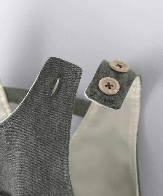 Detalle cierre de tirantes mediante botones OEKO TEX en color beige. El peto Land Baby en sarga denim verde khaki es un diseño en globo, funcional y elegante para tu bebé. www.kala.es