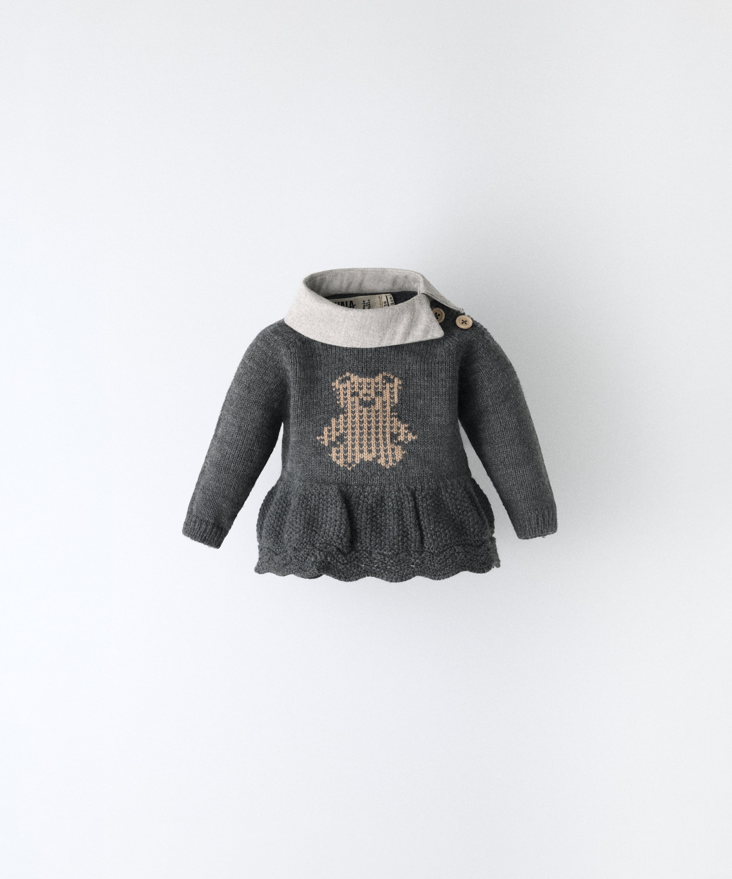 Vestido en punto gris oscuro con oso Kala en intarsia color beige y cuello en sarga gris clara. Apertura en el hombro con botones en tonalidad beige. Ideal para poder vestir a tu bebé. www.kala.es