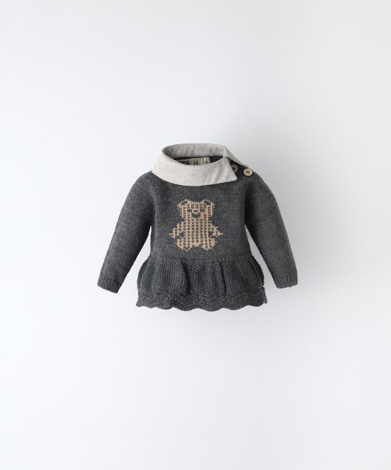 Vestido en punto gris oscuro con oso Kala en intarsia color beige y cuello en sarga gris clara. Apertura en el hombro con botones en tonalidad beige. Ideal para poder vestir a tu bebé. www.kala.es