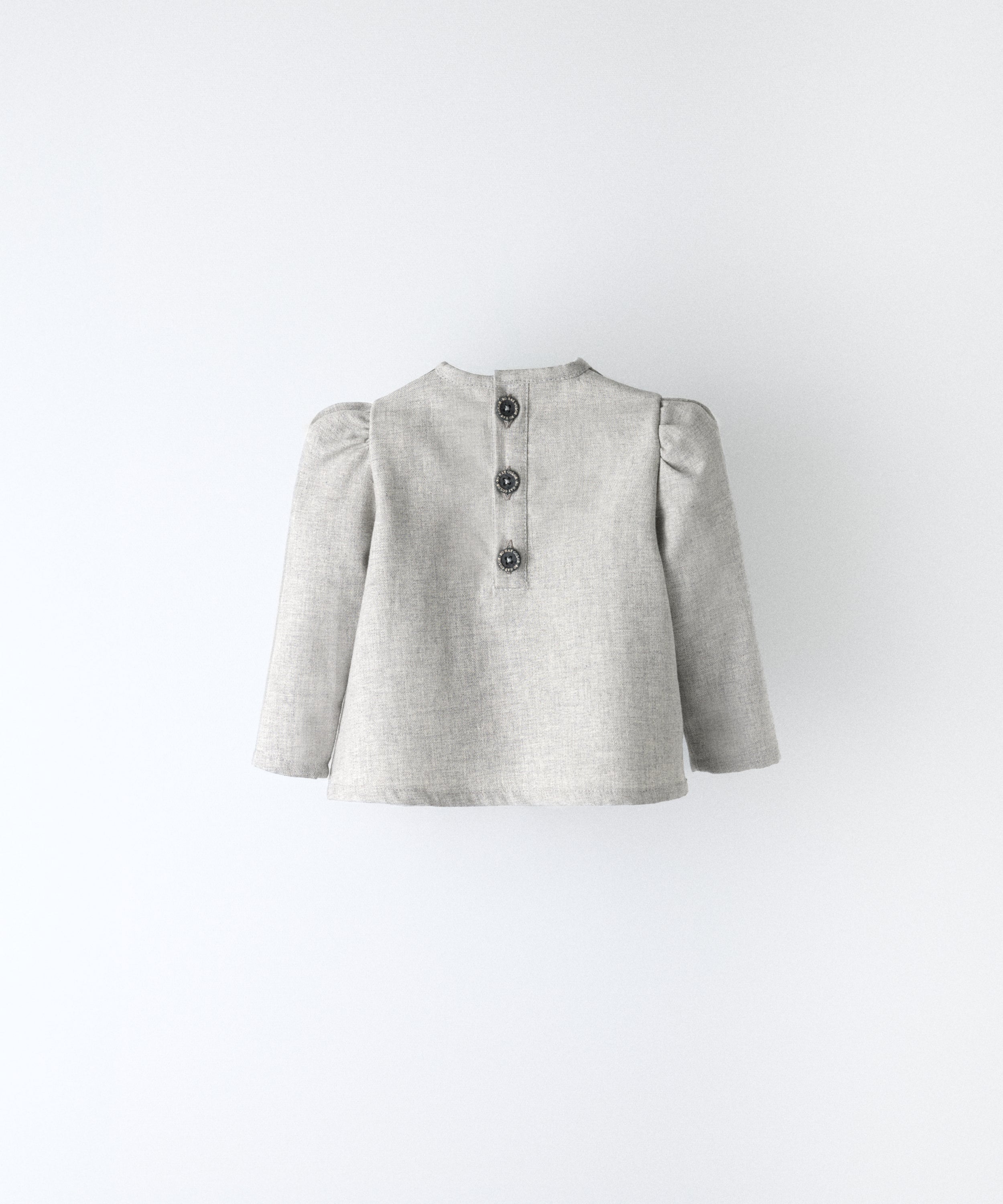 Espalda del blusón gris claro que forma parte del conjunto Harper. Espalda con apertura y cierre con botones OEKO TEX. Mangas largas con volumen en hombro. Delicadeza y estética para los más pequeños. www.kala.es