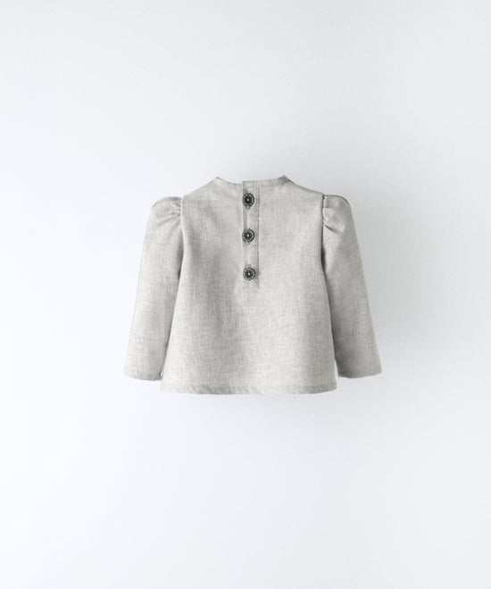 Espalda del blusón gris claro que forma parte del conjunto Harper. Espalda con apertura y cierre con botones OEKO TEX. Mangas largas con volumen en hombro. Delicadeza y estética para los más pequeños. www.kala.es
