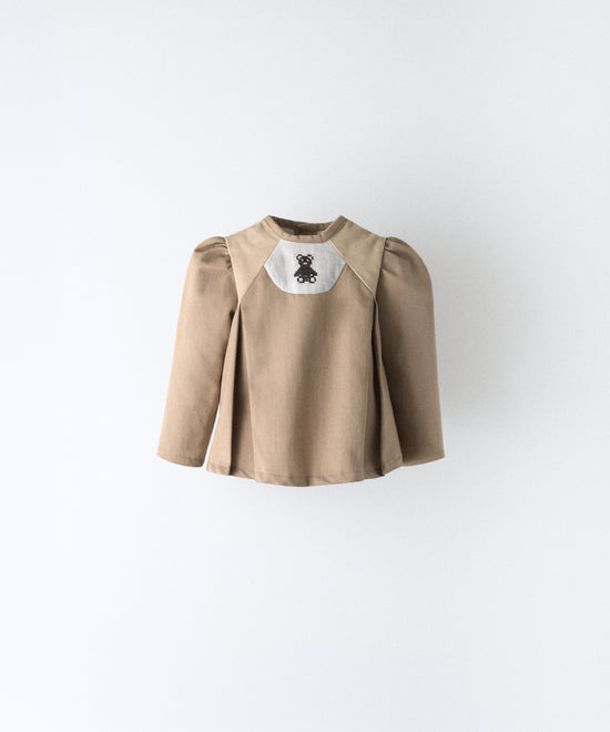Delantero del blusón avellana con toques pana beige que forma parte del Conjunto Harper. Manga larga asentada con volumen en hombro y oso Kala bordado al contraste. Sin querer tu bebé será el centro de las miradas. www.kala.es