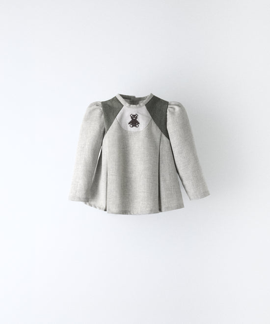 Delantero del blusón gris claro con toques verde khaki que forma parte del Conjunto Harper. Manga larga asentada con volumen en hombro y oso Kala bordado al contraste. Sin querer tu bebé será el centro de las miradas. www.kala.es