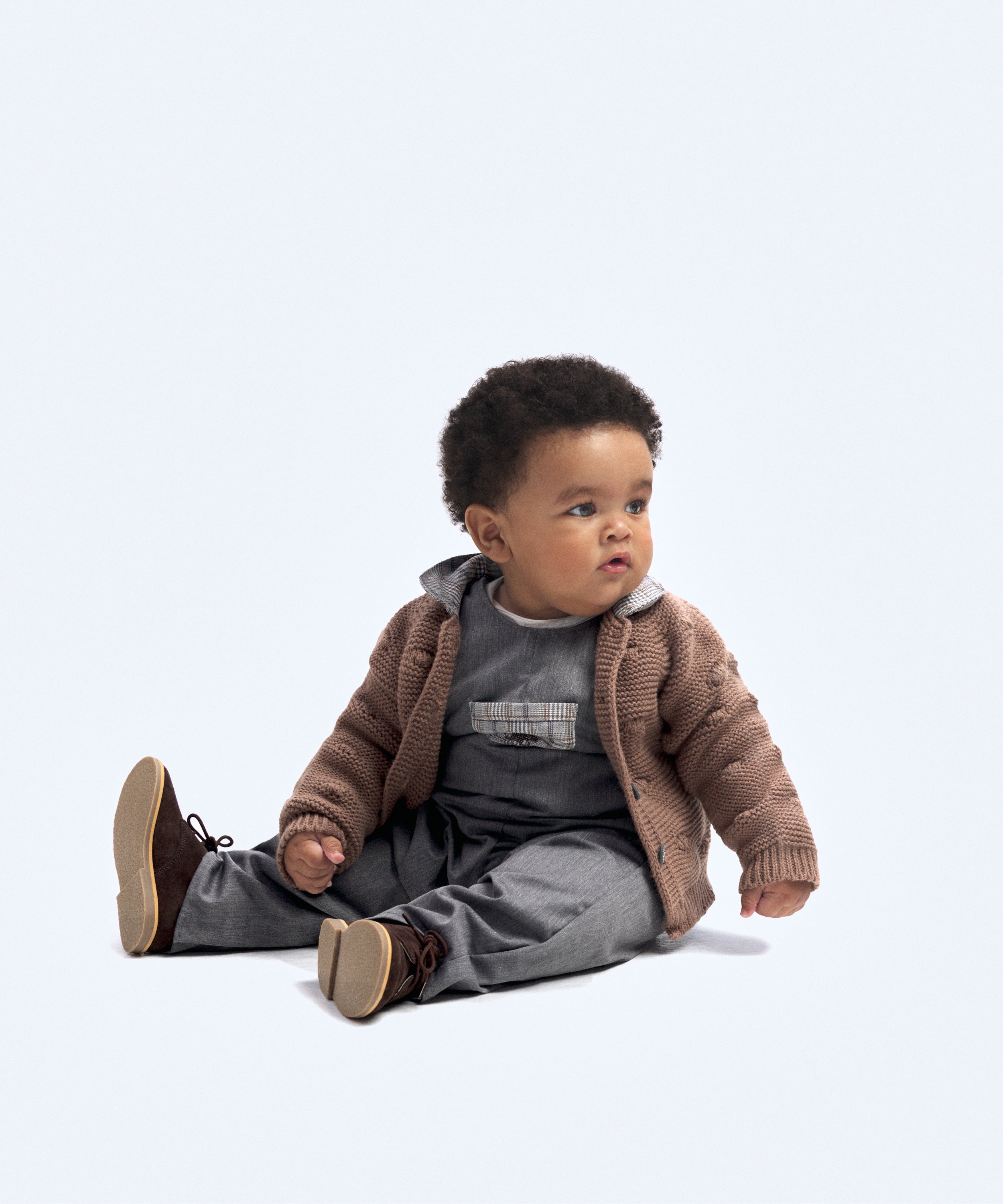 Look de ropa infantil de bebé de Kala. El bebé lleva puesto el Body Liberty en color gris claro, el Peto Land Baby en azul grisáceo y la chaqueta Brunel color marrón y cuello en contraste en tejido de cuadros. Sofisticación, elegancia y atemporalidad para la infancia. 