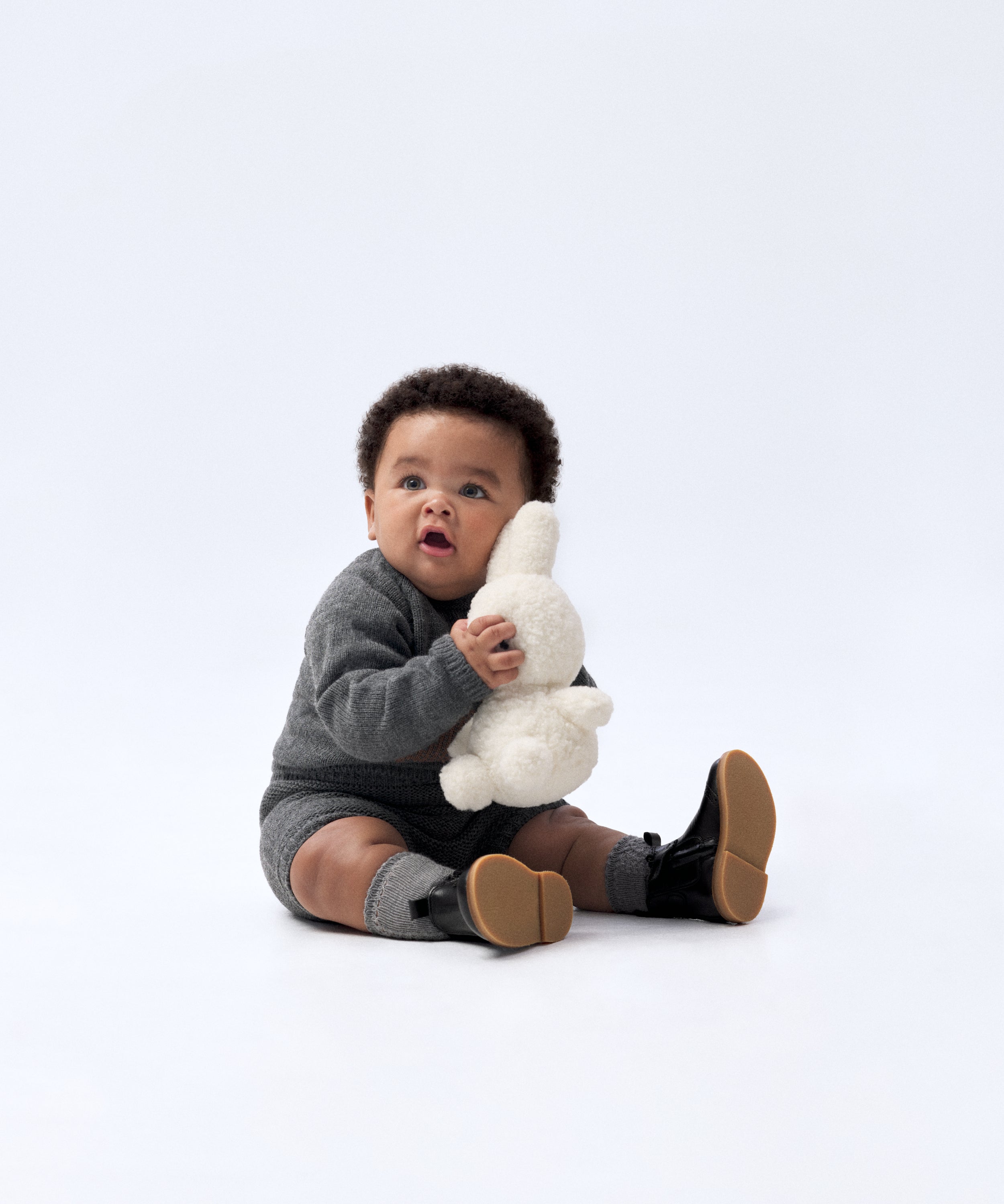 Look de ropa infantil de bebé de Kala. El bebé lleva puesto El conjunto Strutt de punto en color gris oscuro. Compuesto por jersey con oso de Kala en intarsia color marrón y pantalón. Sofisticación y elegancia para la infancia. 