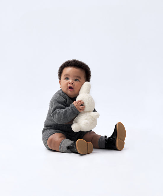 Look de ropa infantil de bebé de Kala. El bebé lleva puesto El conjunto Strutt de punto en color gris oscuro. Compuesto por jersey con oso de Kala en intarsia color marrón y pantalón. Sofisticación y elegancia para la infancia. 