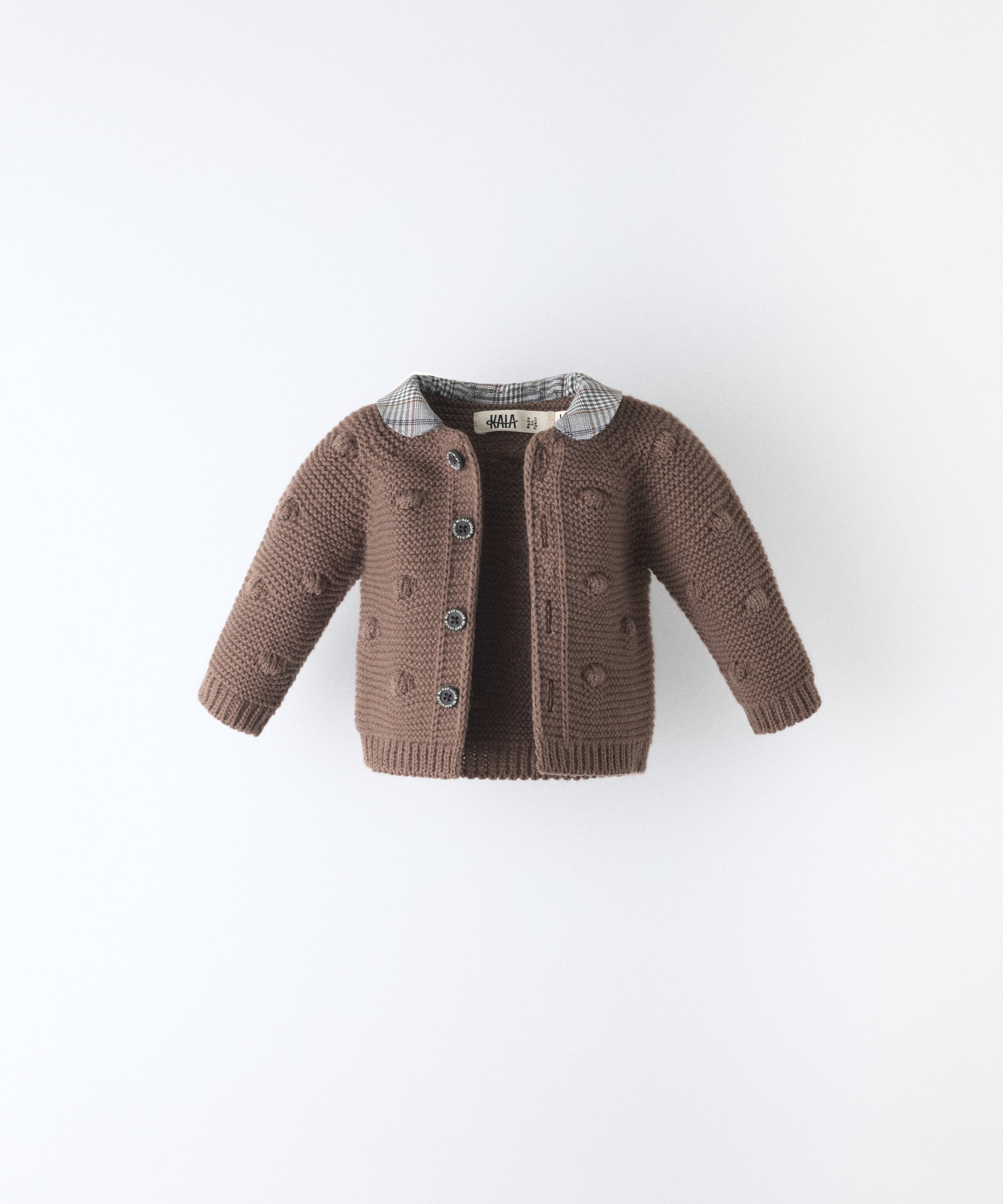 La Chaqueta Brunel marrón en punto acrilico con bodoques, botones OEKO TEX y cuello contrastado con tejido cuadros con certificación GRS. www.kala.es