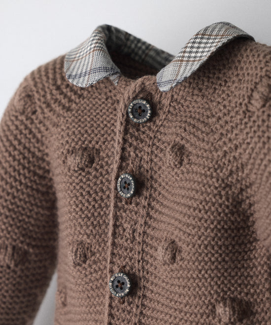 Detalle de los botones OEKO TEX de La Chaqueta Brunel marrón en punto acrilico con bodoques. Cuello contrastado con tejido cuadros con certificación GRS. Esta chaqueta de bebé celebra la unión entre tradición y diseño contemporáneo.www.kala.es