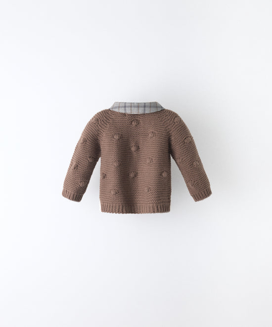 Espalda de La Chaqueta Brunel marrón para bebé  en punto acrílico. Textura de bodoques y cuello contrastado en tejido de cuadros con certificación GRS. www.kala.es