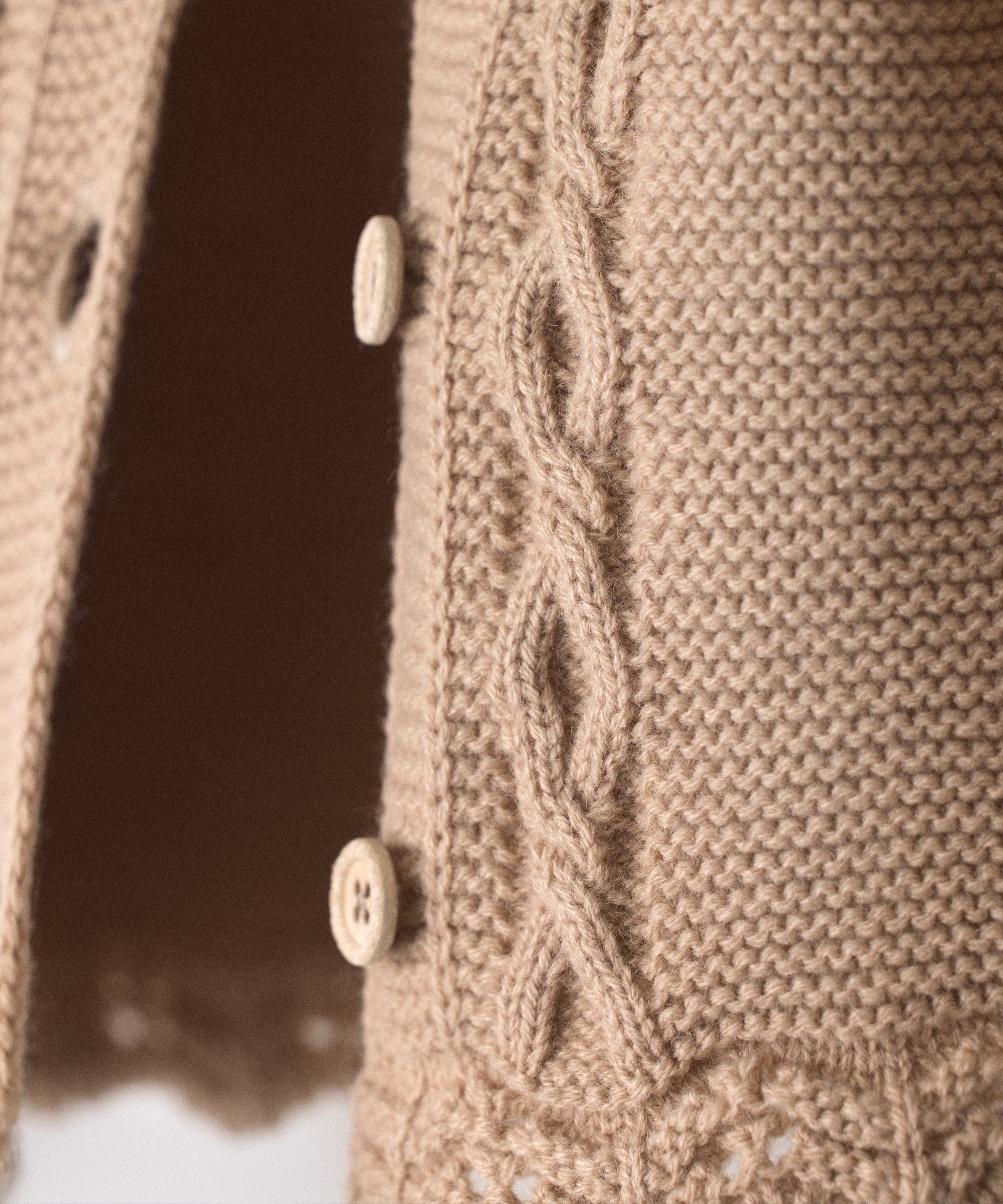 Detalle de trenzas en relieve en el delantero al tono de La Chaqueta Jolly en punto acrílico y color beige. Cierre con botones OEKO TEX al tono. Elegancia y artesanía para tu bebé. 