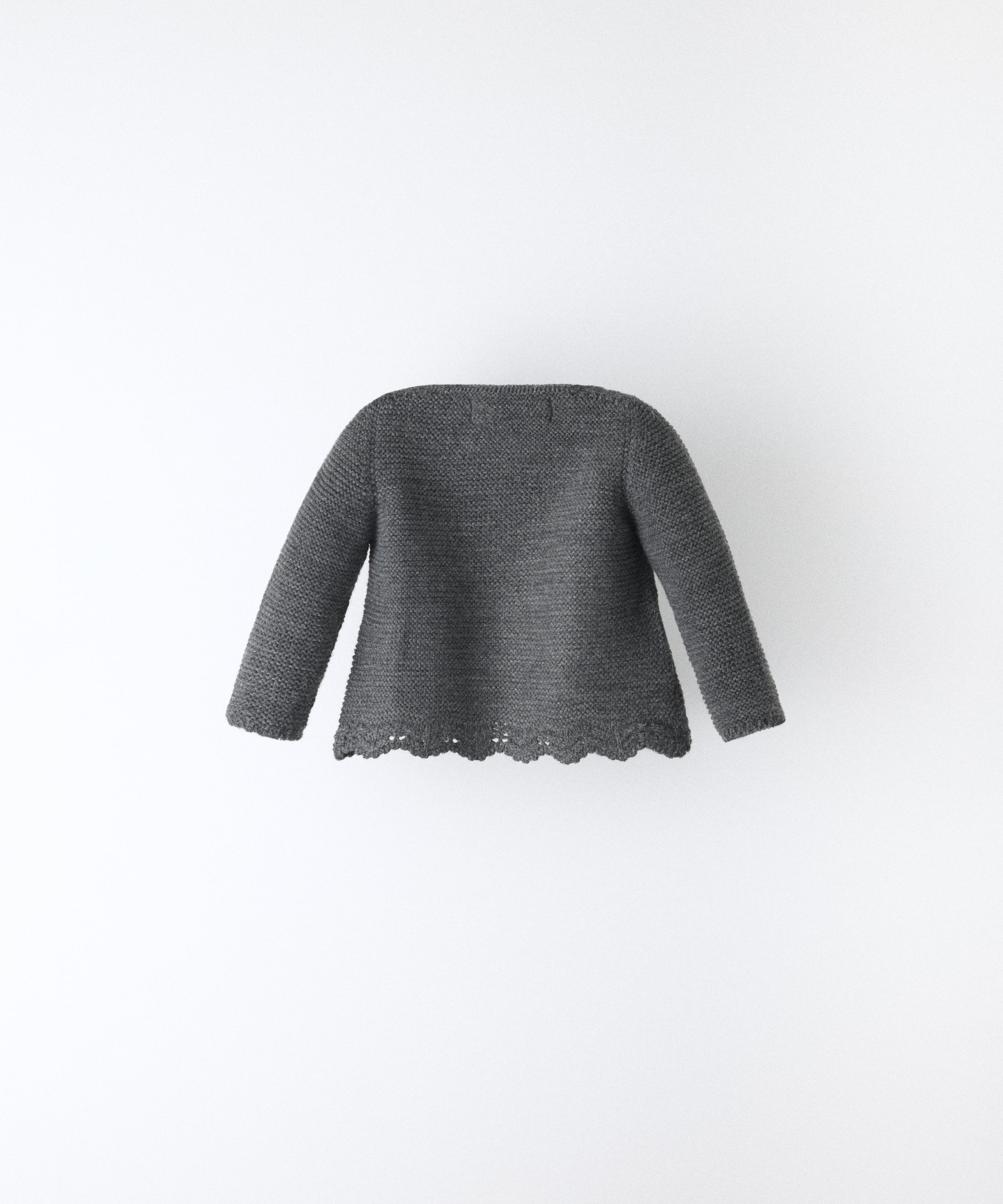 Espalda de la Chaqueta Jolly en punto acrílico y color gris oscuro con bajo ondulado y detalle de trenzas en relieve en el delantero al tono. Elegancia y artesanía para tu bebé. www.kala.es