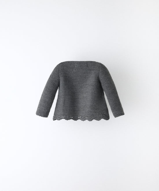 Espalda de la Chaqueta Jolly en punto acrílico y color gris oscuro con bajo ondulado y detalle de trenzas en relieve en el delantero al tono. Elegancia y artesanía para tu bebé. www.kala.es