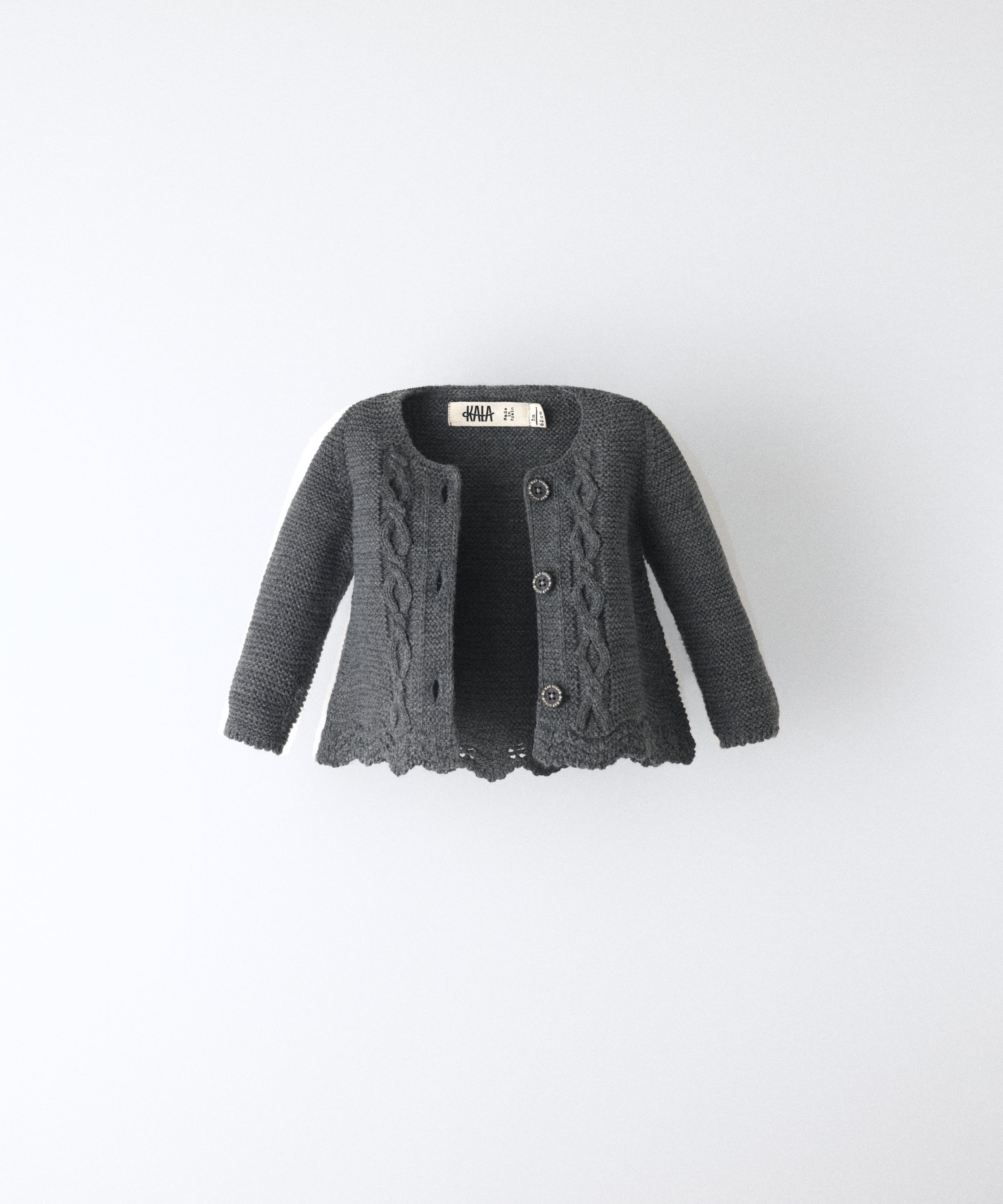 La Chaqueta Jolly en punto acrílico y color gris oscuro con bajo ondulado y detalle de trenzas en relieve en el delantero al tono. Elegancia y artesanía para tu bebé. 