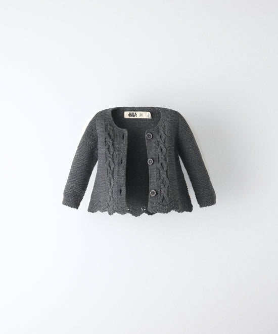 La Chaqueta Jolly en punto acrílico y color gris oscuro con bajo ondulado y detalle de trenzas en relieve en el delantero al tono. Elegancia y artesanía para tu bebé. 
