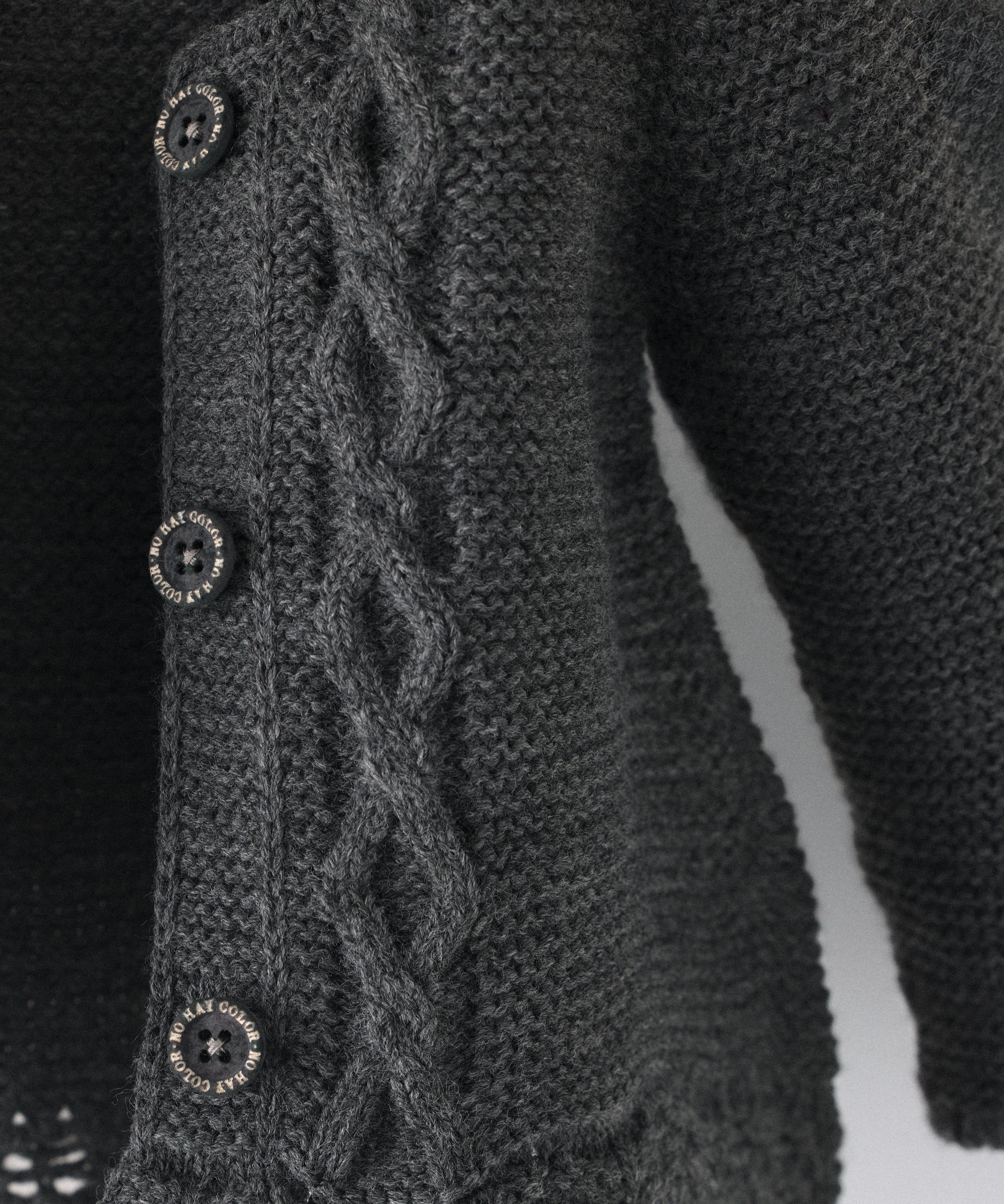 Detalle de trenzas en relieve en el delantero al tono de La Chaqueta Jolly en punto acrílico y color gris oscuro. Cierre con botones OEKO TEX al tono. Elegancia y artesanía para tu bebé. 