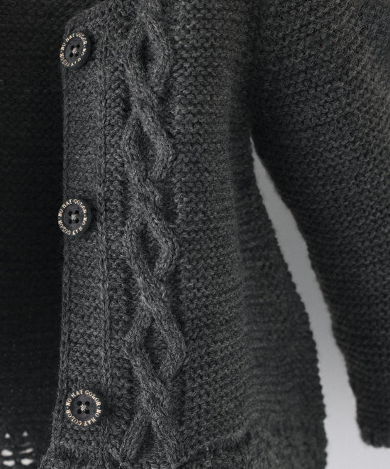 Detalle de trenzas en relieve en el delantero al tono de La Chaqueta Jolly en punto acrílico y color gris oscuro. Cierre con botones OEKO TEX al tono. Elegancia y artesanía para tu bebé. 