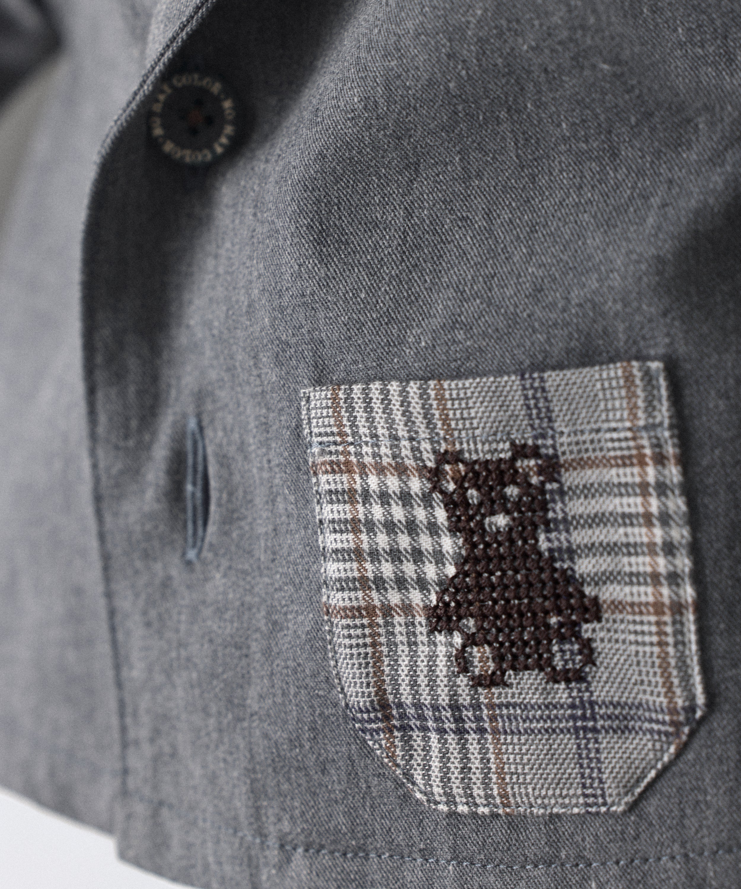 Detalle del bolsillo a cuadros con oso Kala bordado de La Chaqueta Lily gris azulada, una americana para tu bebé para celebrar la infancia. Una prenda que combina diseño estructurado y materiales nobles con una visión de atemporalidad funcional, celebra la valentía de lo simple. Confeccionada en sarga denim certificada GRS y forro 100% algodón. www.kala.es