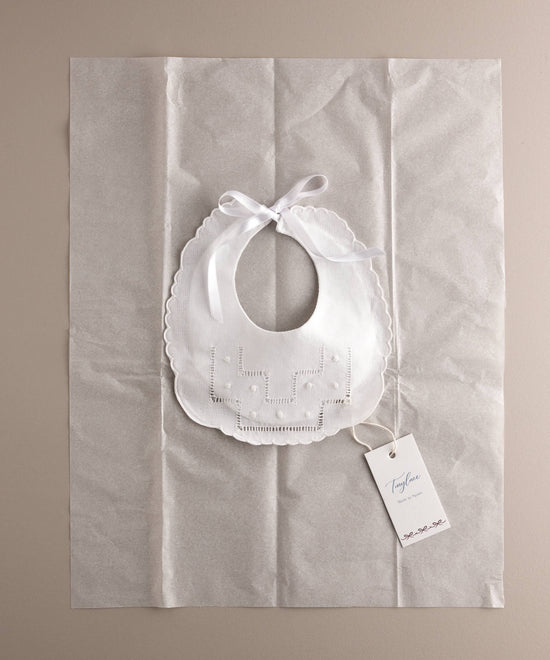Babero recién nacido de algodón bordado con escalera de vainica y bodoque sobre papel seda y etiqueta marca a modo de packaging. Ref 8648W