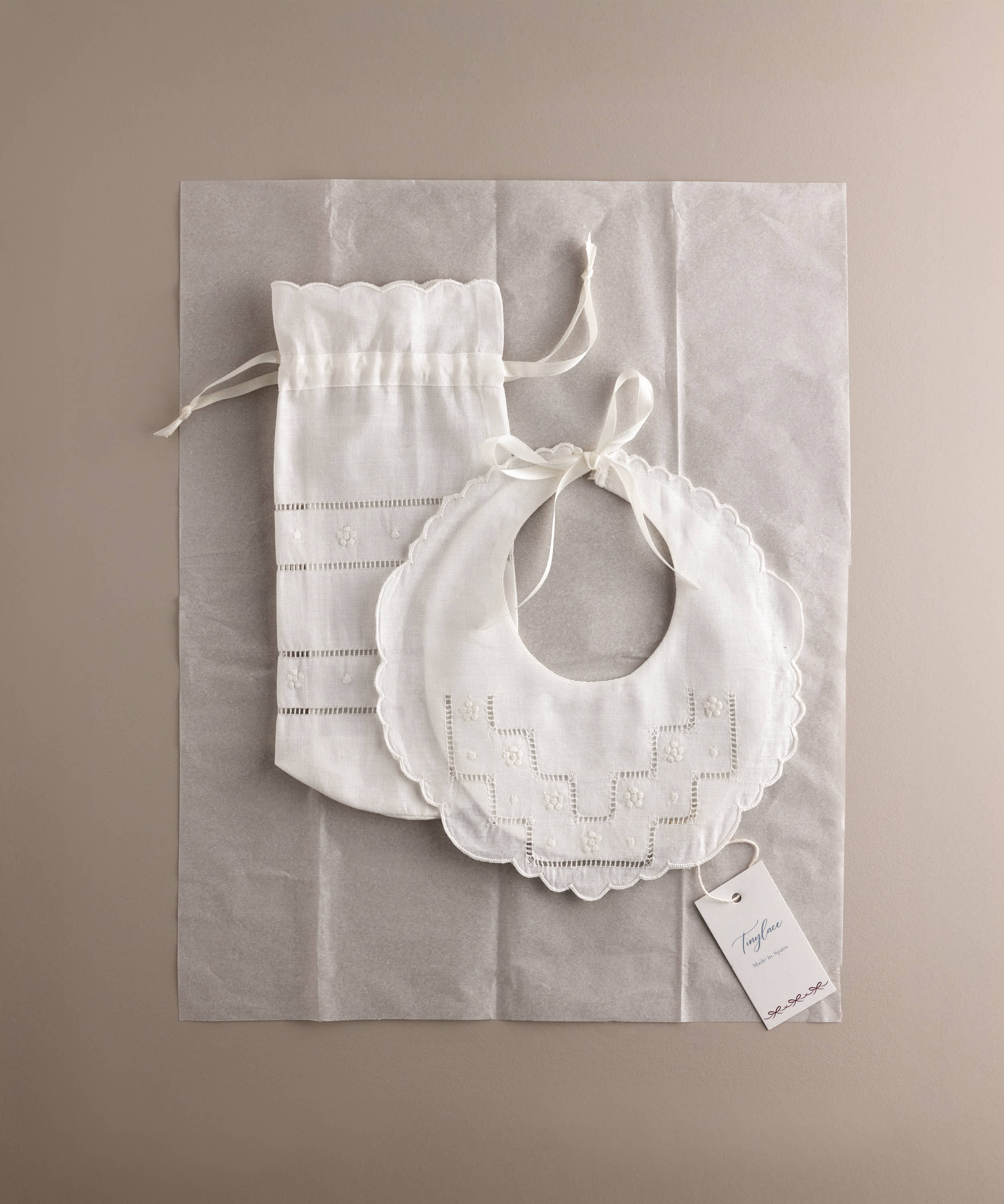 Set babero y portabiberón de lino bordado flor presentado sobre papel de seda con etiqueta de marca estilo packaging editorial