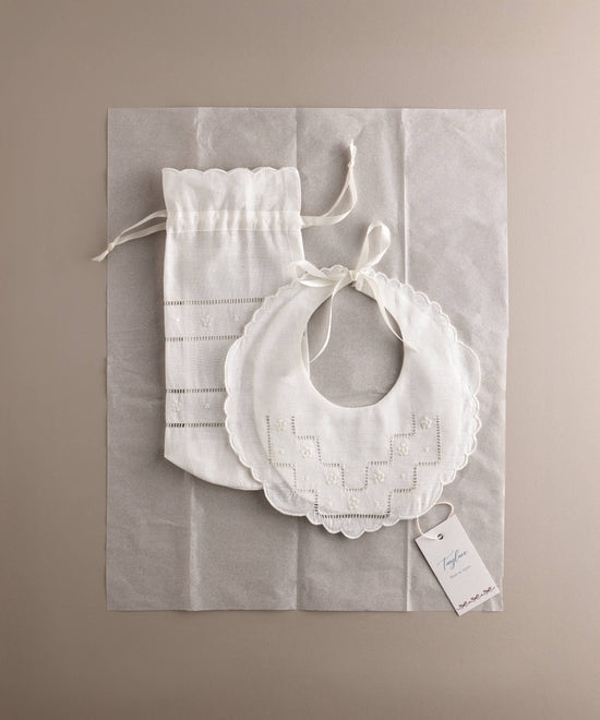 Set babero y portabiberón de lino bordado flor presentado sobre papel de seda con etiqueta de marca estilo packaging editorial