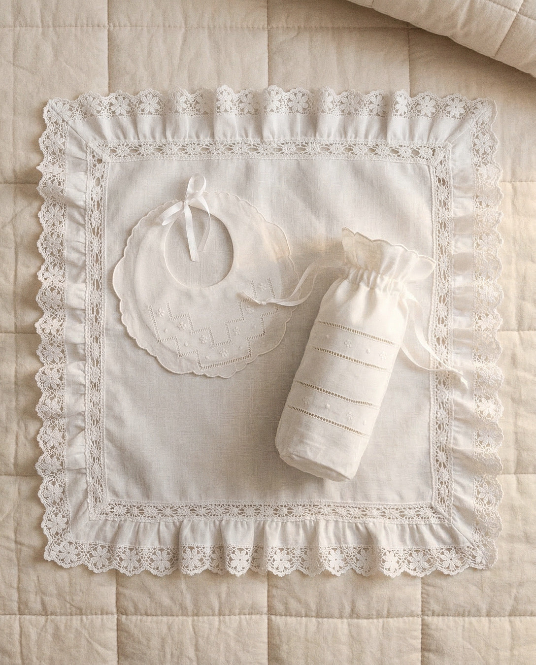 Set babero y porta biberón de lino bordado flor sobre cama y arrullo